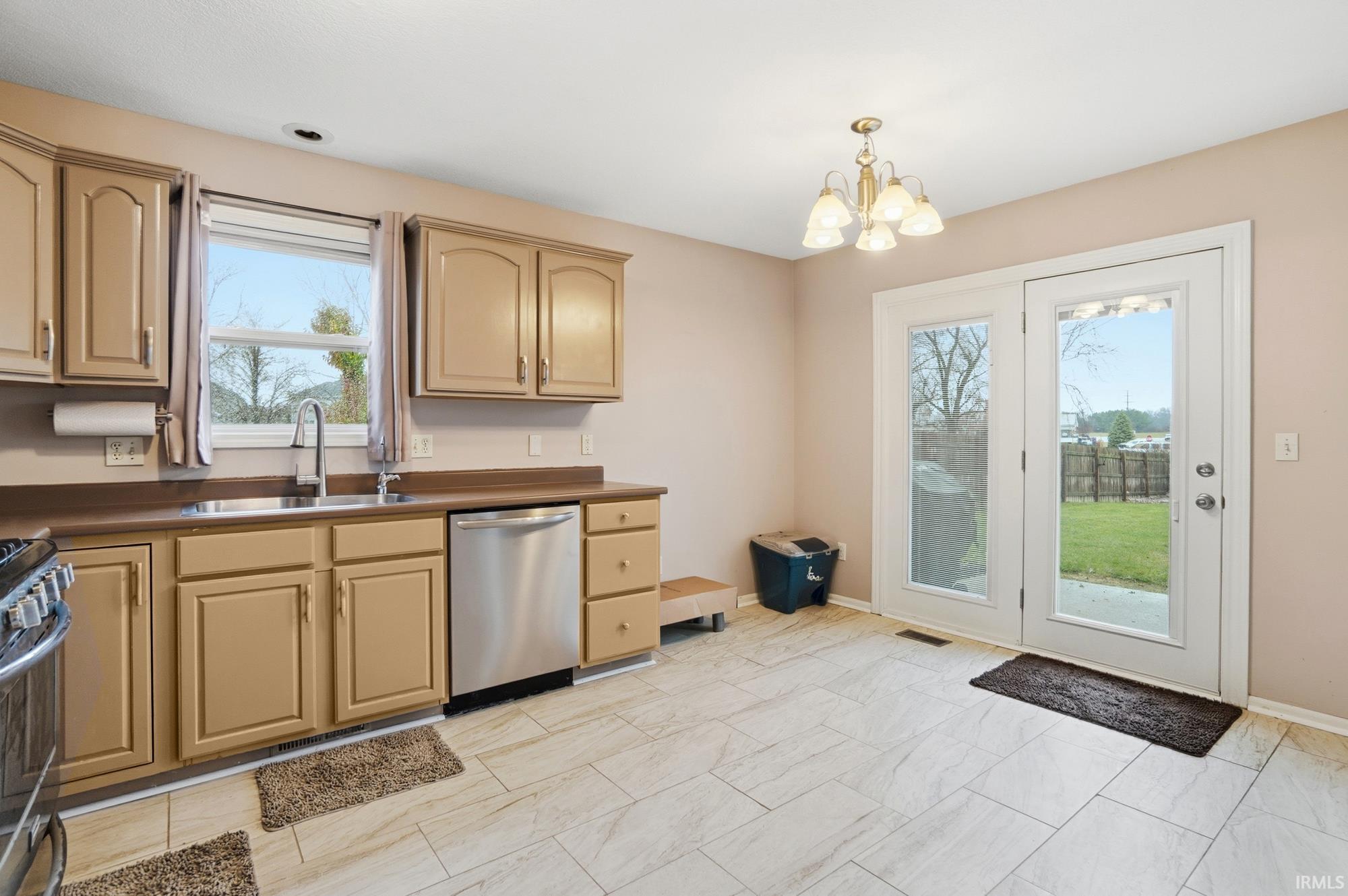 Kitchen with dark countertops, stainless steel appliances, a chandelier, decorative light fixtures, and light brown cabinets