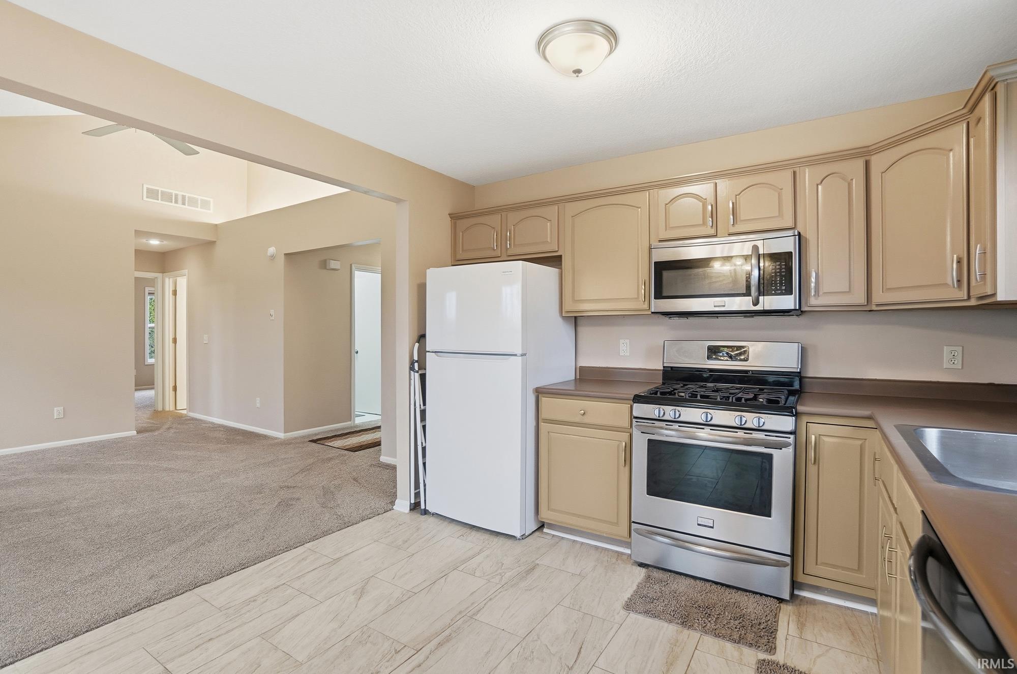 Kitchen with appliances with stainless steel finishes, cream cabinetry, and light carpet