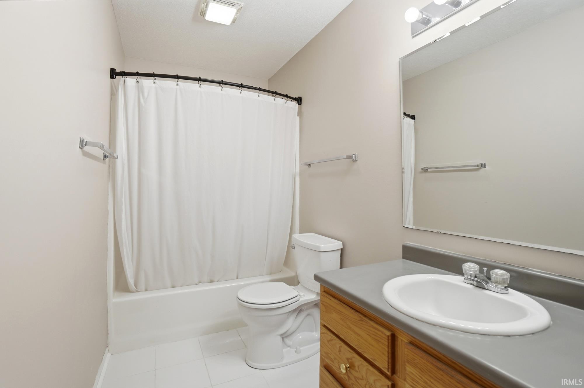 Bathroom with shower / bathtub combination with curtain, vanity, and light tile patterned floors