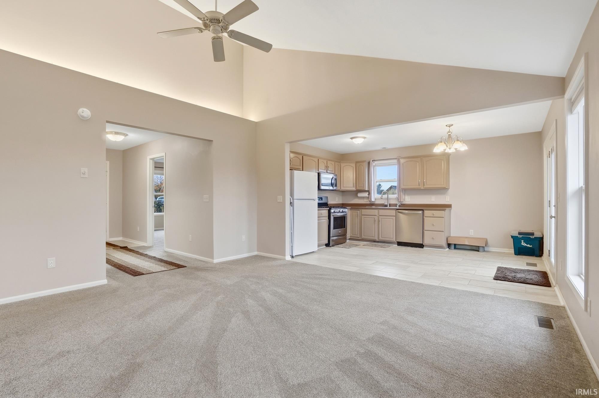Unfurnished living room featuring light carpet, a chandelier, ceiling fan, and high vaulted ceiling