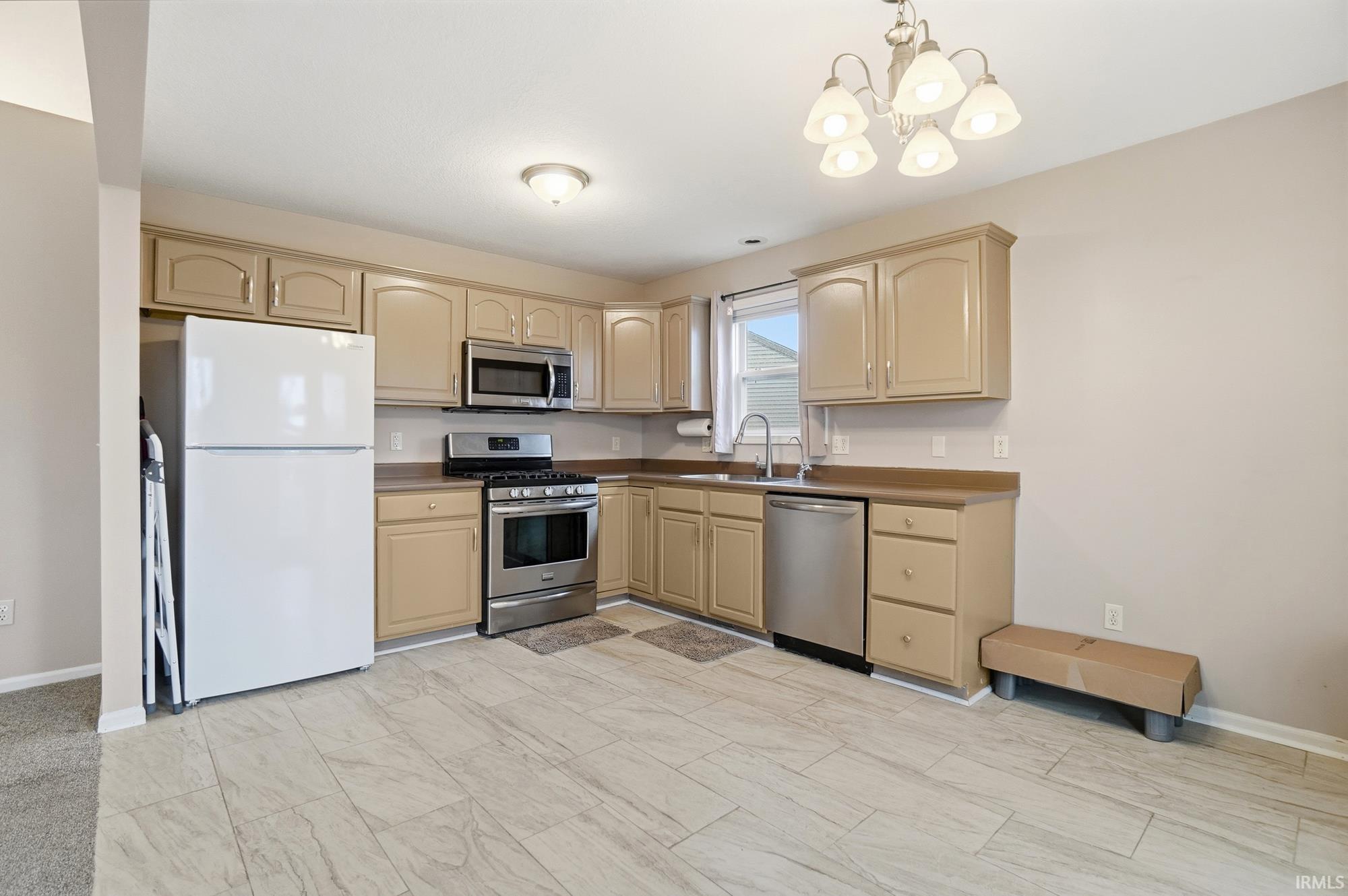 Kitchen featuring appliances with stainless steel finishes, decorative light fixtures, a chandelier, cream cabinetry, and dark countertops