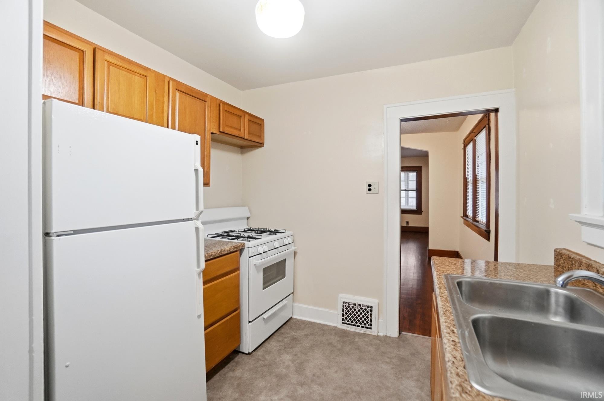 Kitchen featuring white appliances, light carpet, and brown cabinetry