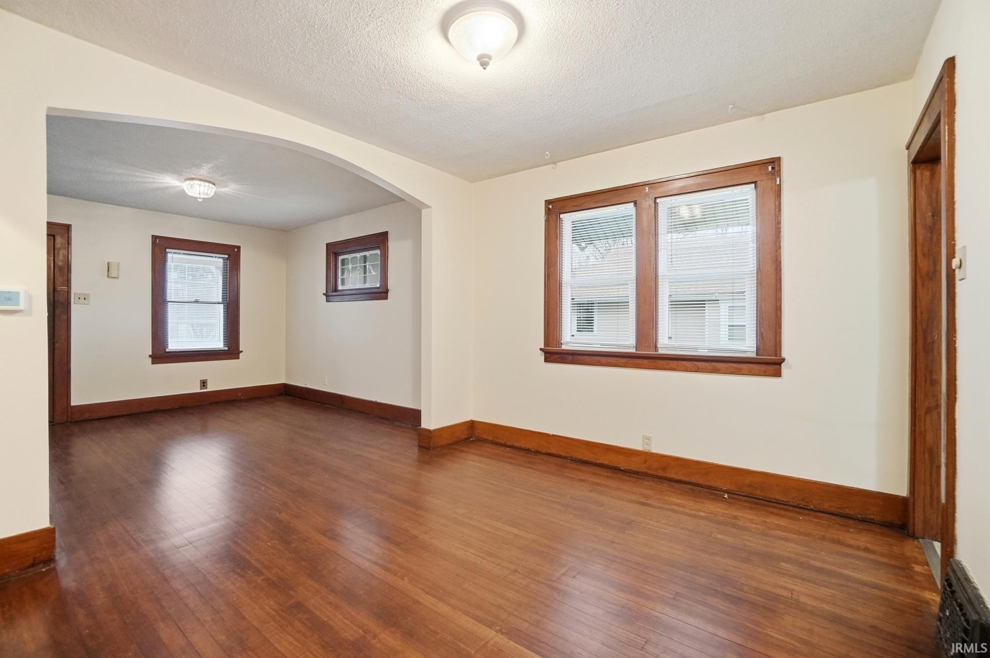 Spare room with arched walkways, wood-type flooring, and a textured ceiling