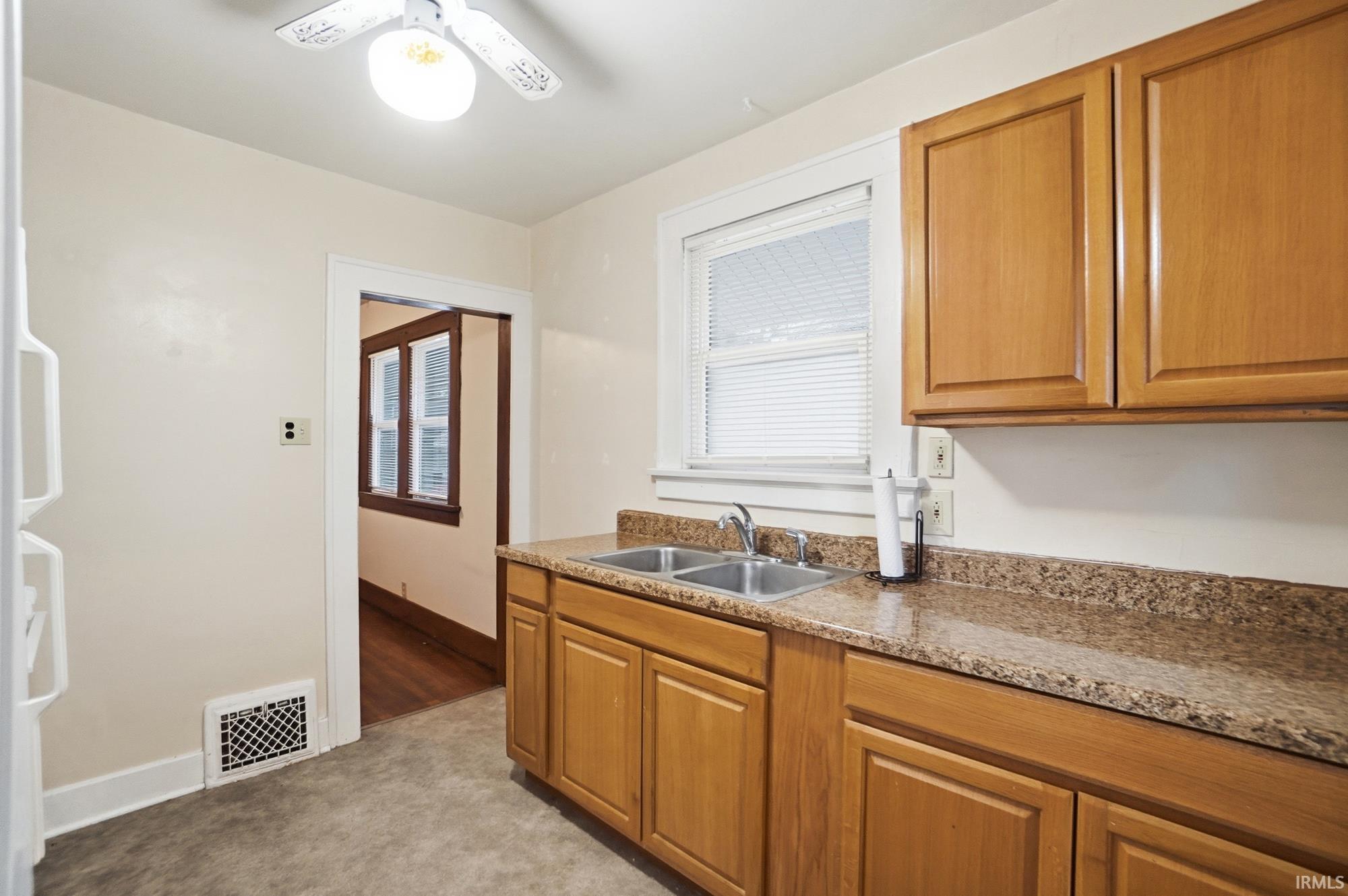 Kitchen with brown cabinets, light colored carpet, freestanding refrigerator, and a ceiling fan