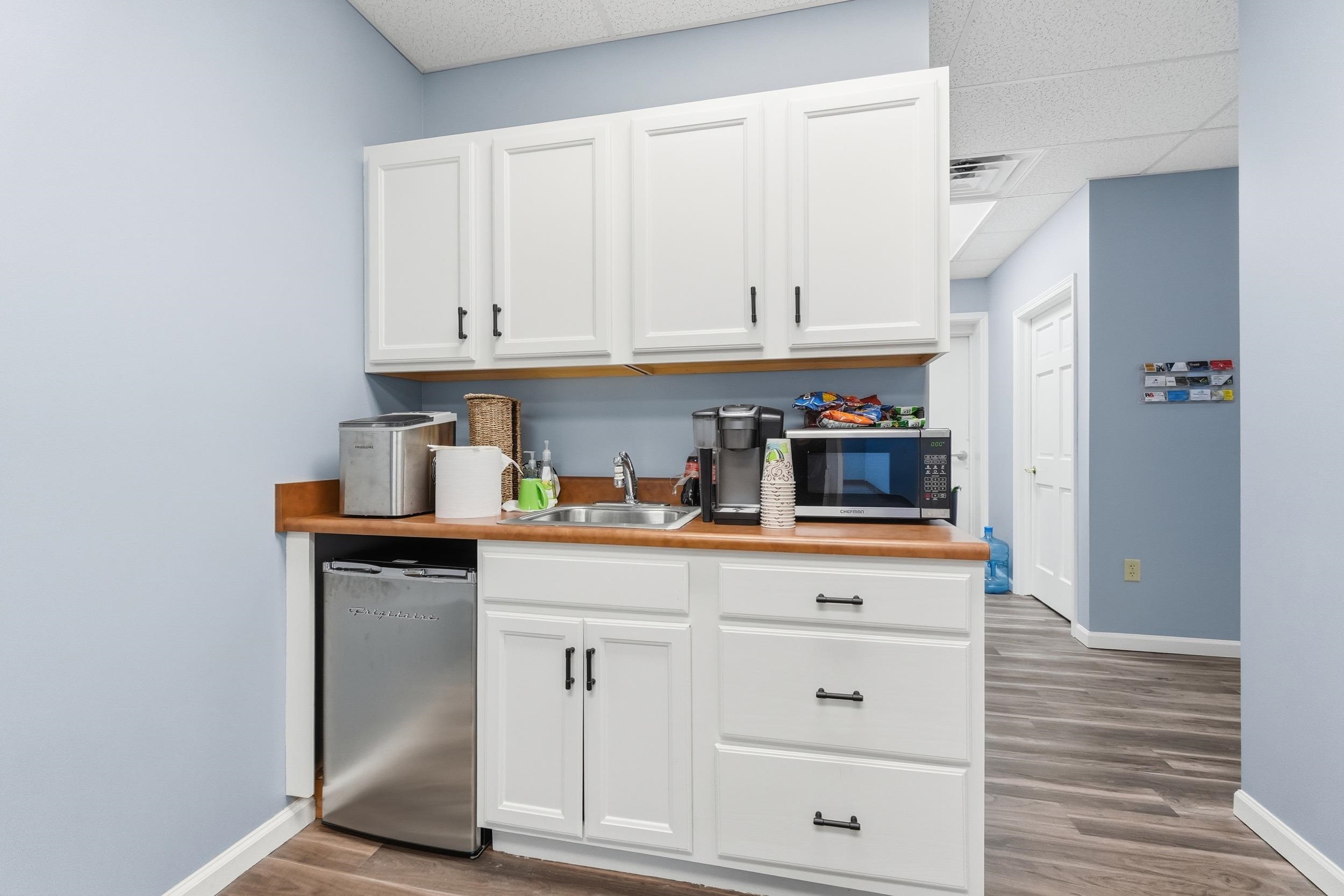 Kitchen with white cabinets, light countertops, light wood-type flooring, and a drop ceiling