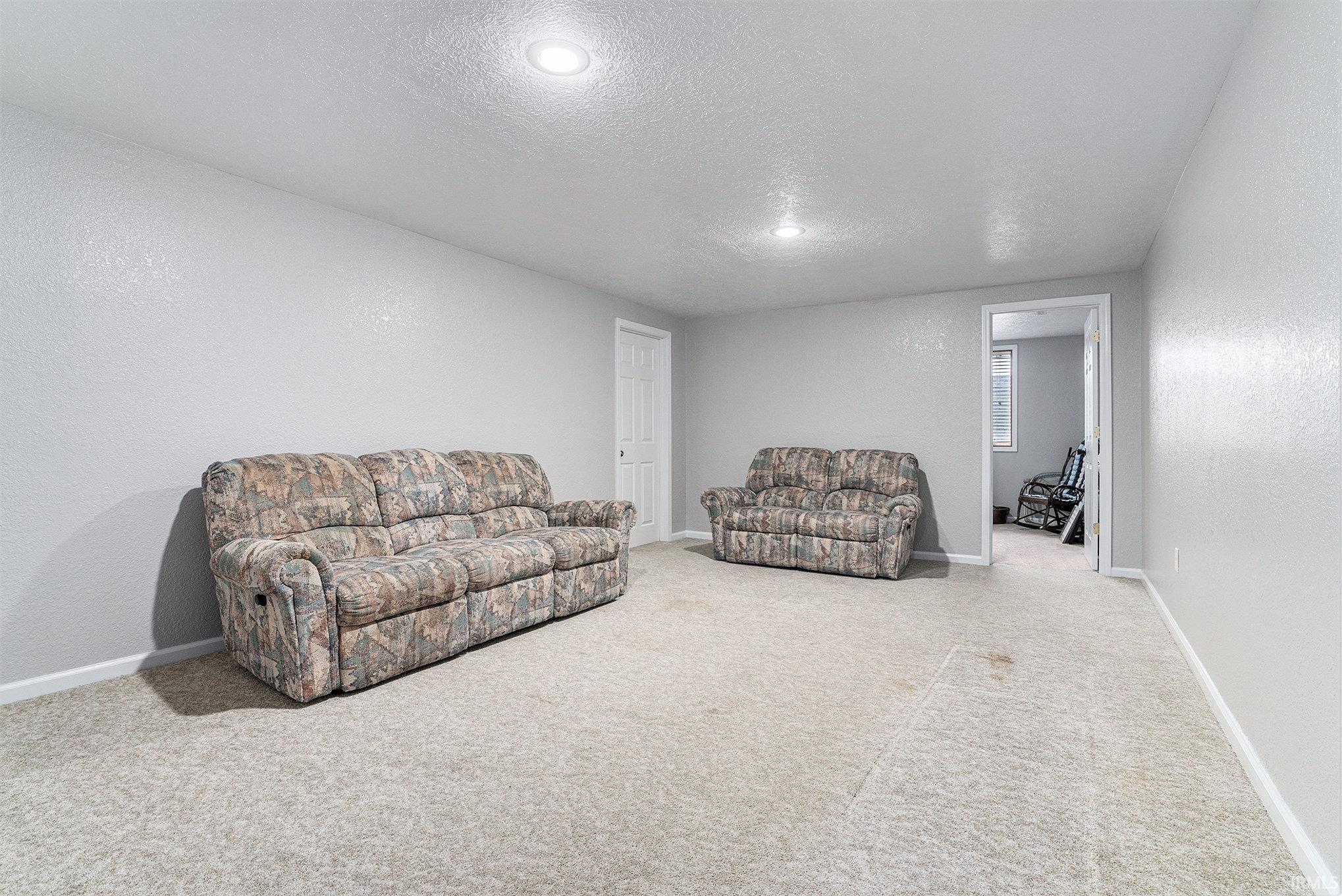 Carpeted living room featuring a textured wall, a textured ceiling, and recessed lighting
