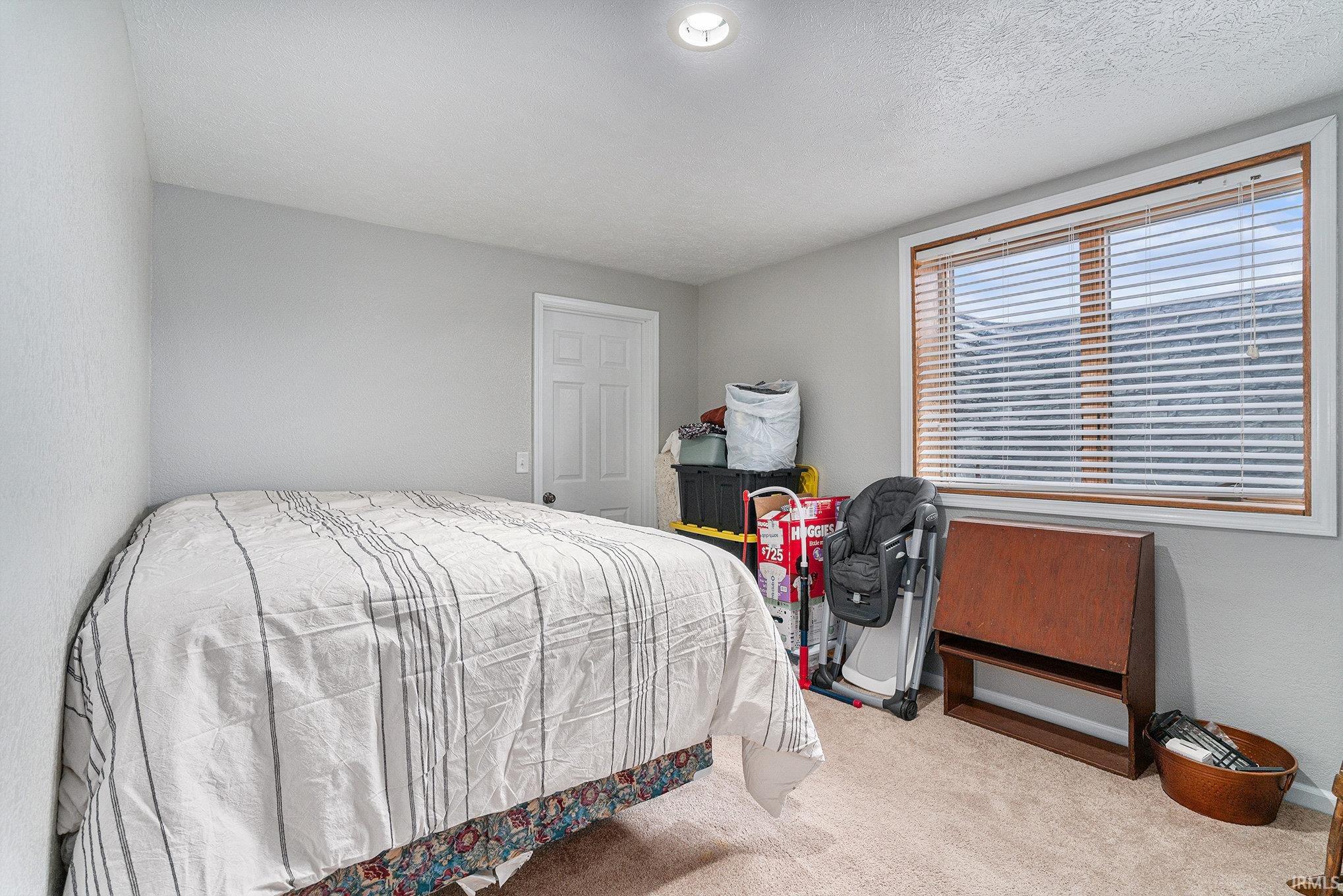 Bedroom with carpet flooring, a textured ceiling, and a textured wall