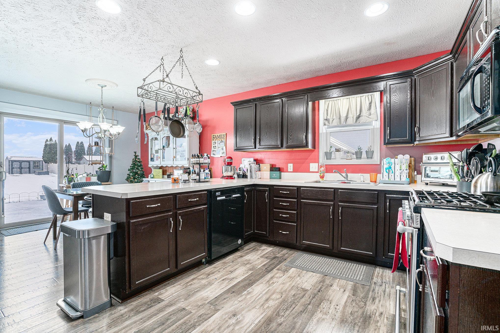 Kitchen featuring a peninsula, light countertops, black appliances, a textured ceiling, and light wood-style flooring