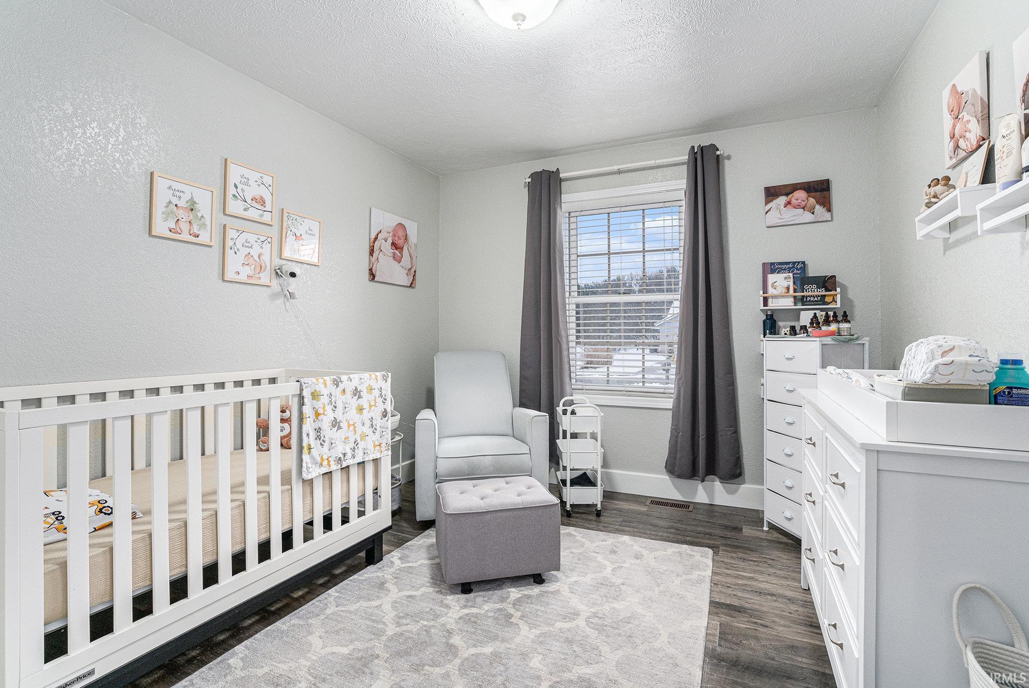 Bedroom featuring a textured ceiling, a crib, dark wood-style flooring, and a textured wall