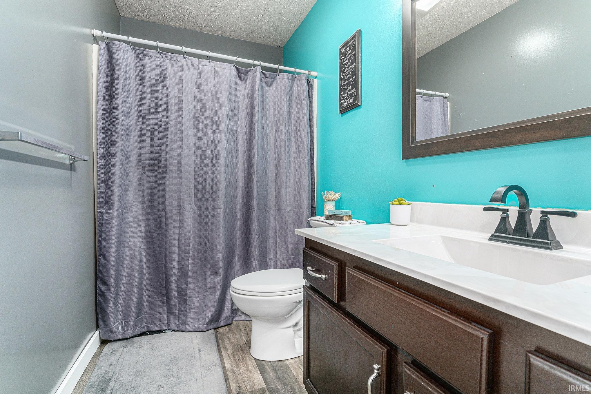 Full bathroom featuring a shower with curtain, vanity, light wood-style flooring, and a textured ceiling