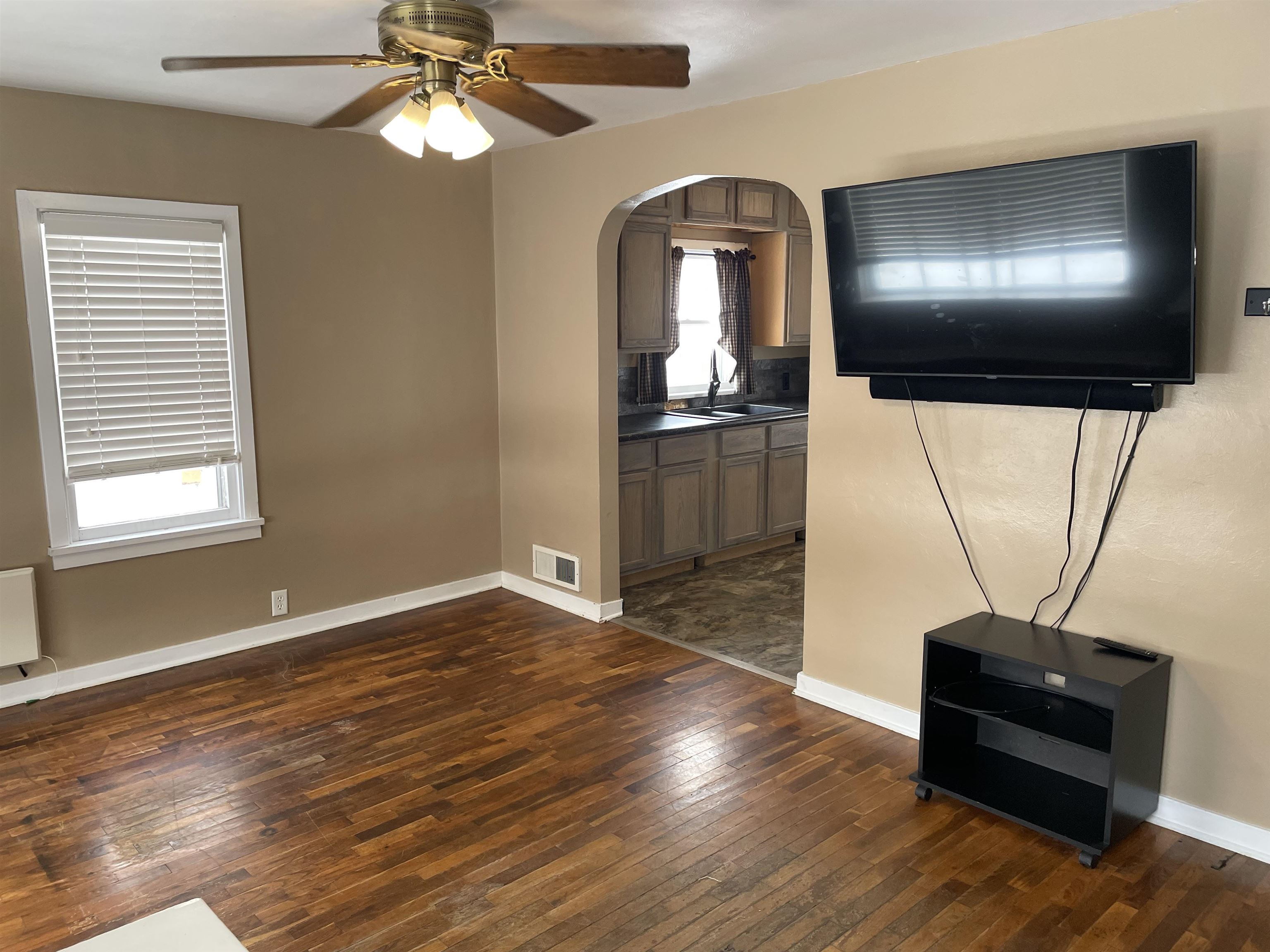 Unfurnished living room featuring arched walkways, ceiling fan, and dark wood finished floors