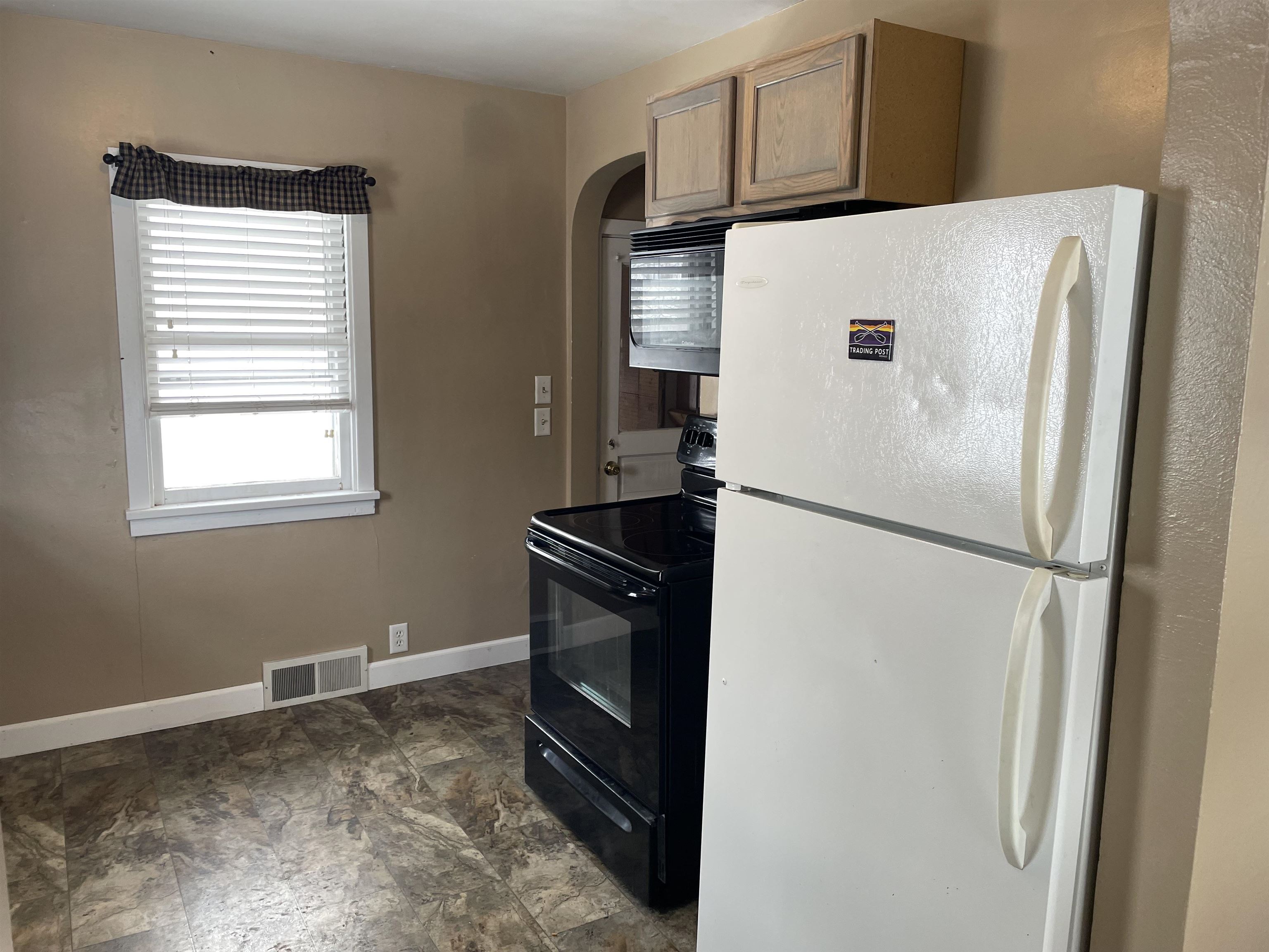 Kitchen featuring freestanding refrigerator, black electric range oven, arched walkways, and stone finish flooring