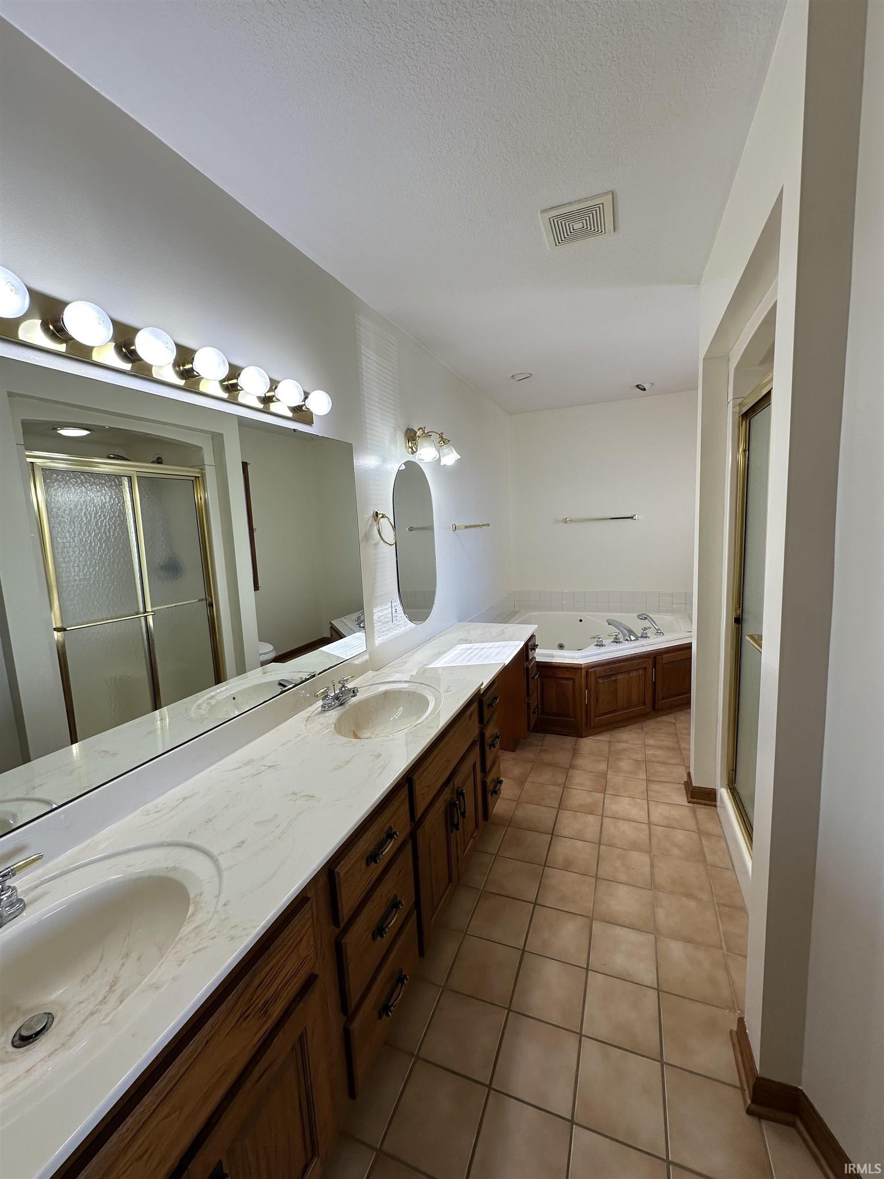 Full bathroom featuring double vanity, light tile patterned floors, a jetted tub, a shower stall, and a textured ceiling