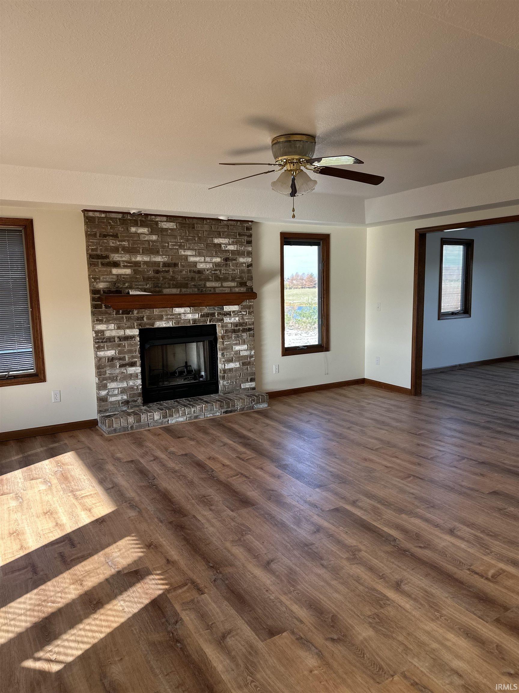 Unfurnished living room featuring a fireplace, a textured ceiling, ceiling fan, and dark wood-type flooring
