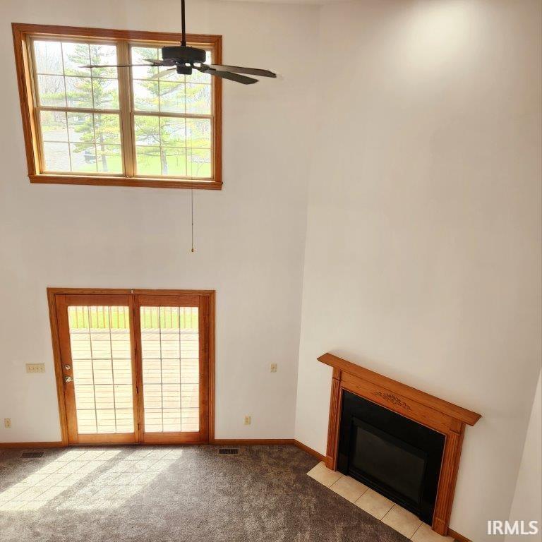 Unfurnished living room featuring plenty of natural light, a towering ceiling, carpet floors, a fireplace with flush hearth, and a ceiling fan