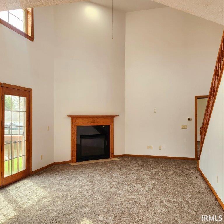 Unfurnished living room featuring a towering ceiling, carpet floors, a fireplace with flush hearth, and a textured ceiling
