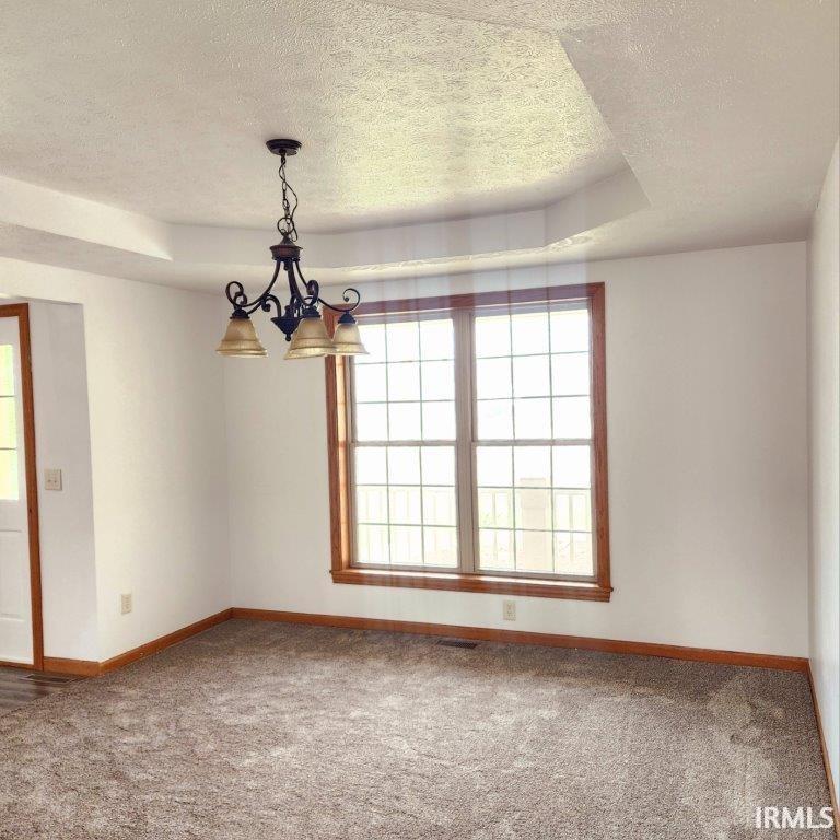 Unfurnished room featuring a raised ceiling, a textured ceiling, carpet flooring, and a chandelier