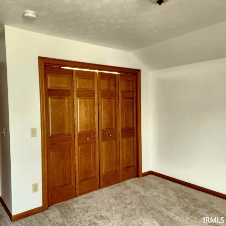 Unfurnished bedroom with carpet flooring, a closet, and vaulted ceiling