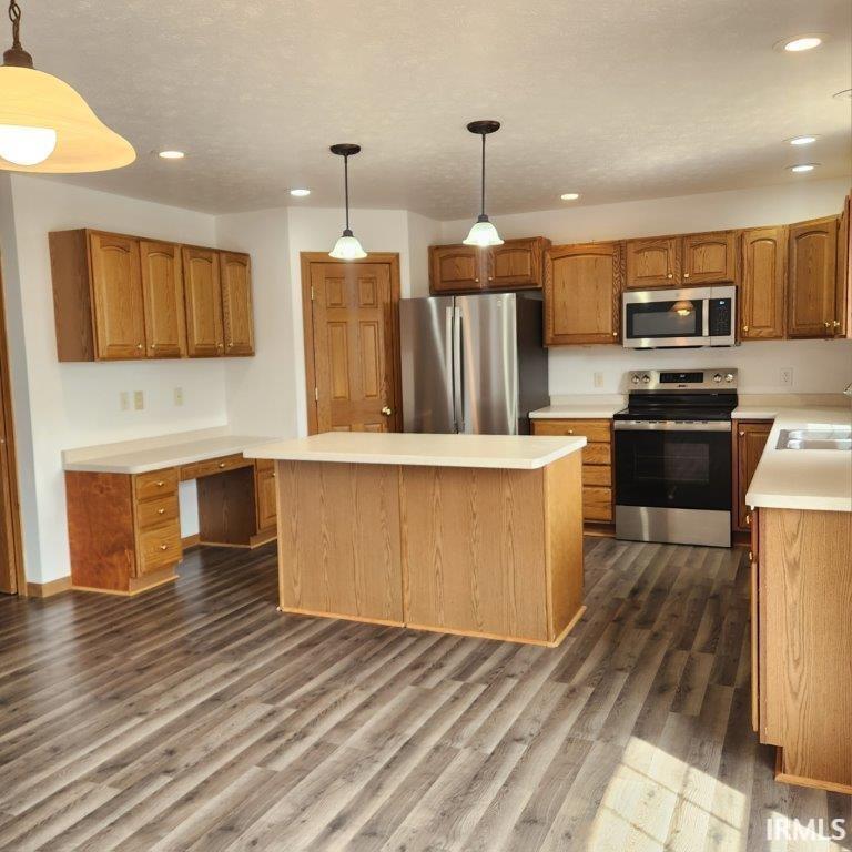 Kitchen with stainless steel appliances, decorative light fixtures, light countertops, a kitchen island, and built in study area