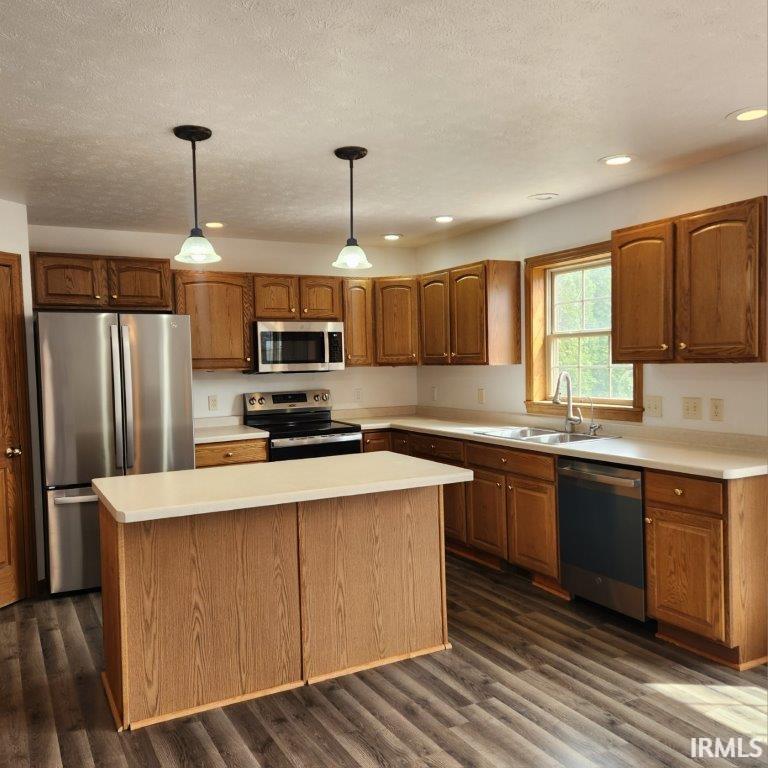 Kitchen featuring stainless steel appliances, a center island, pendant lighting, brown cabinetry, and light countertops