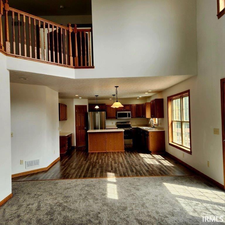 Kitchen with a towering ceiling, hanging light fixtures, light countertops, a center island, and dark wood-style flooring