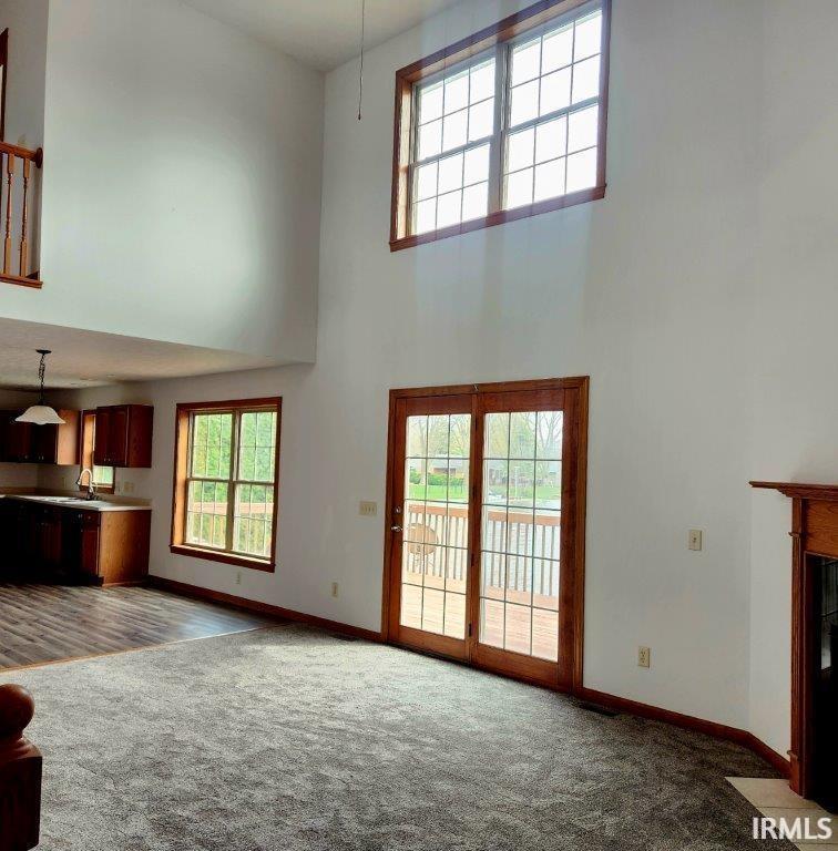 Unfurnished living room with a high ceiling, dark carpet, and a fireplace with flush hearth