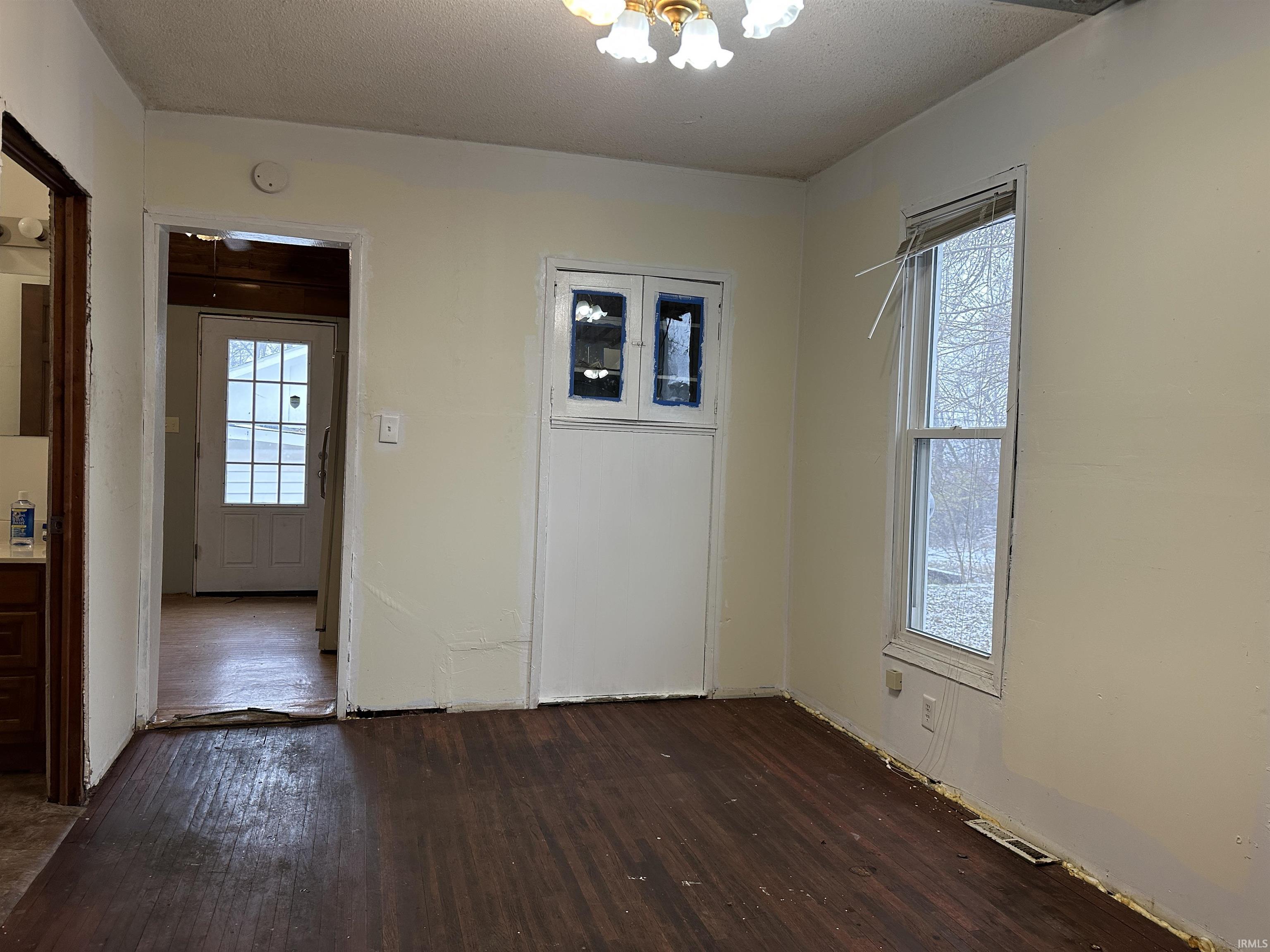 Spare room featuring dark wood finished floors, a chandelier, and a textured ceiling