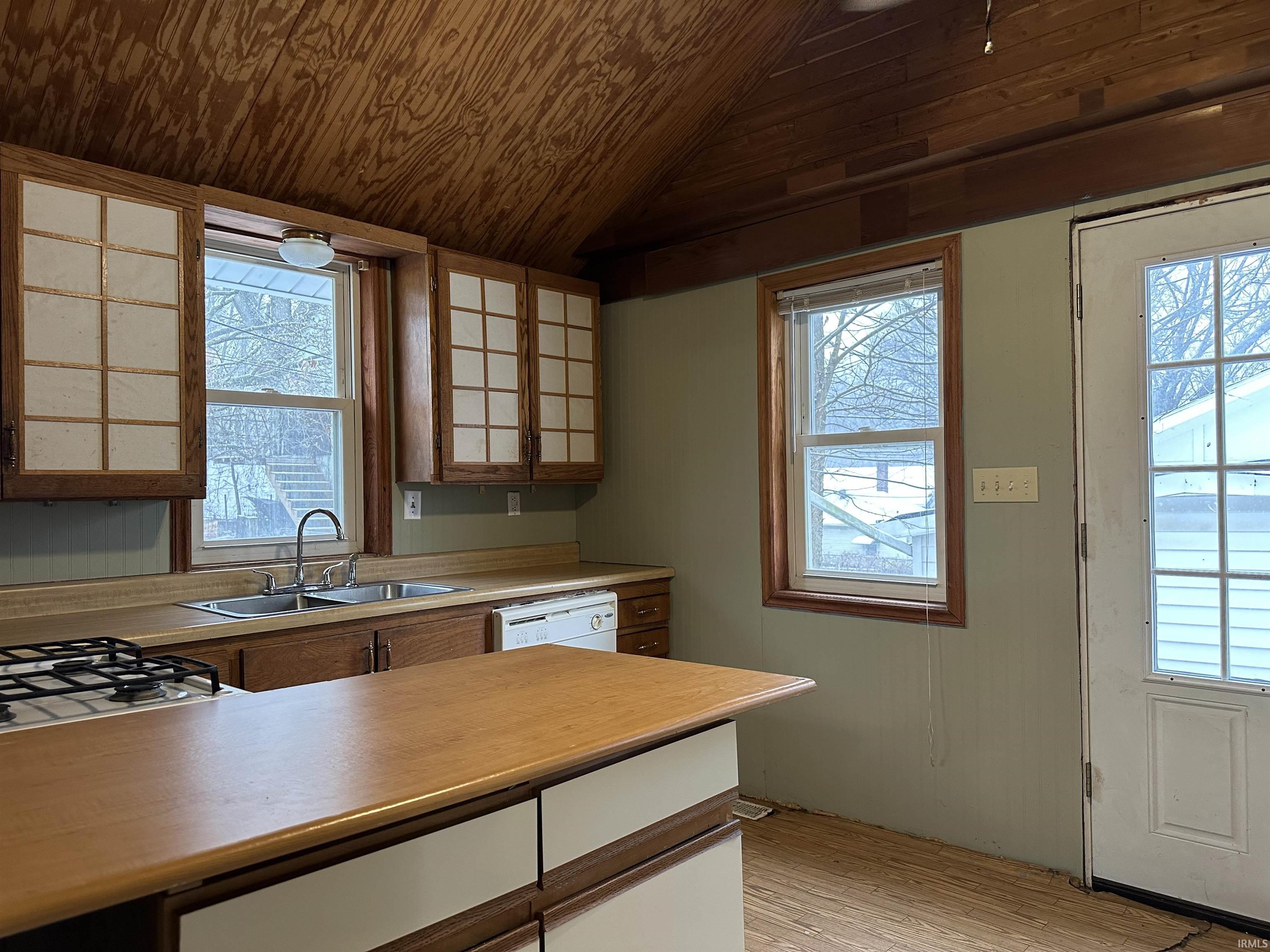 Kitchen featuring light countertops, vaulted ceiling, light wood finished floors, brown cabinetry, and white dishwasher