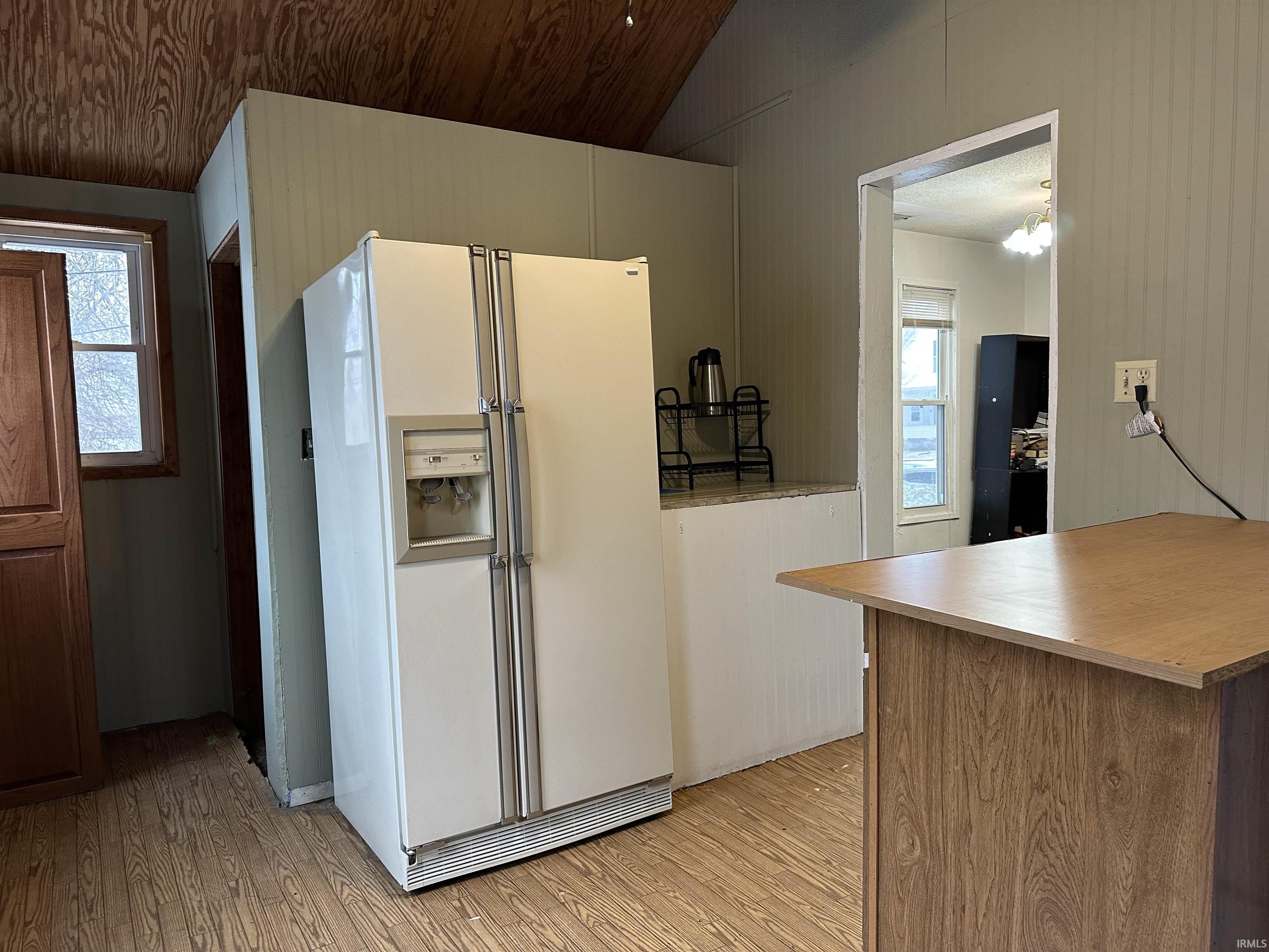 Kitchen featuring white fridge with ice dispenser, lofted ceiling, light wood finished floors, light countertops, and wooden walls