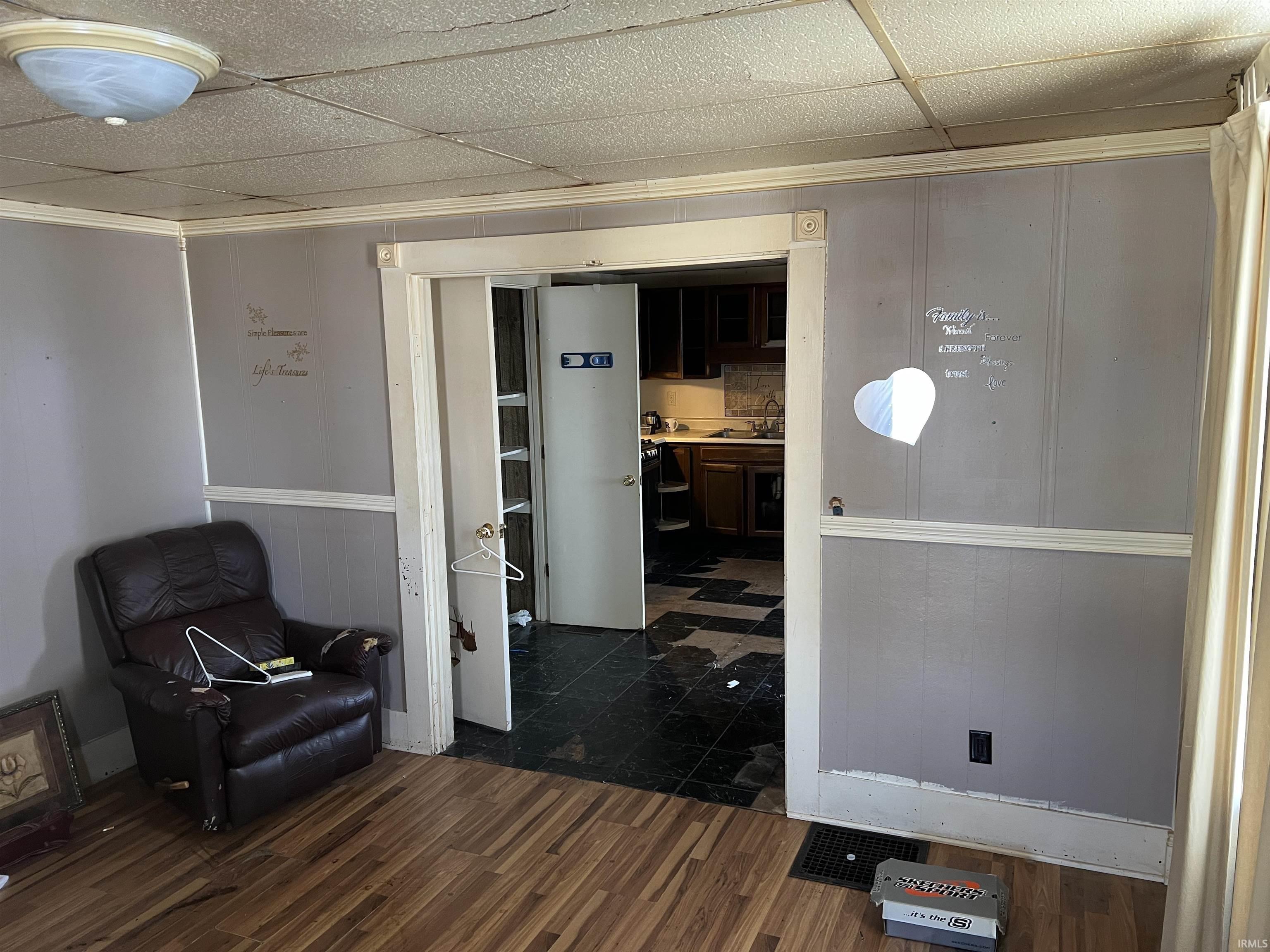 Living area featuring dark wood-style flooring, a wainscoted wall, wood walls, ornamental molding, and a drop ceiling