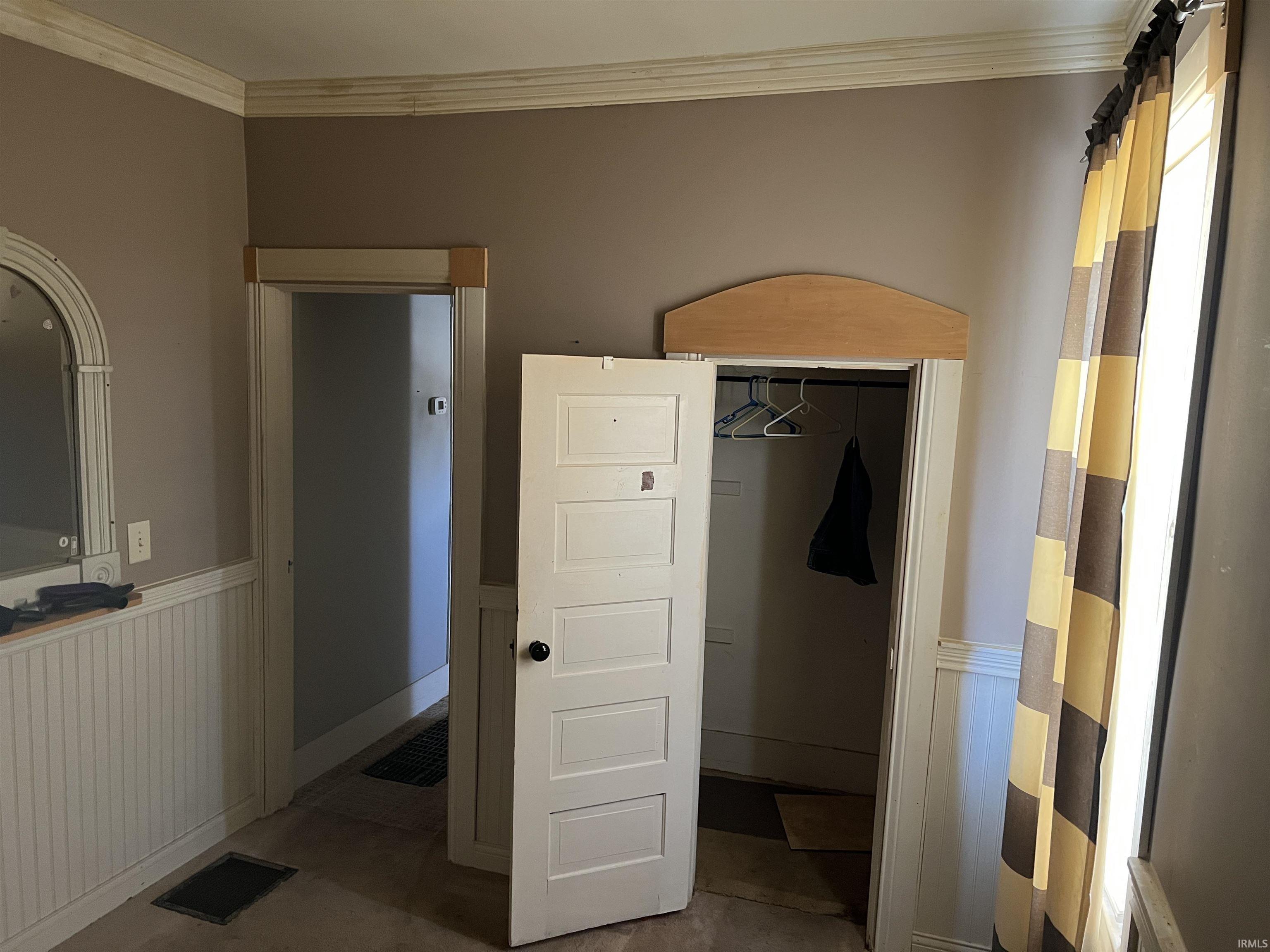 Unfurnished bedroom with a wainscoted wall, crown molding, and a closet