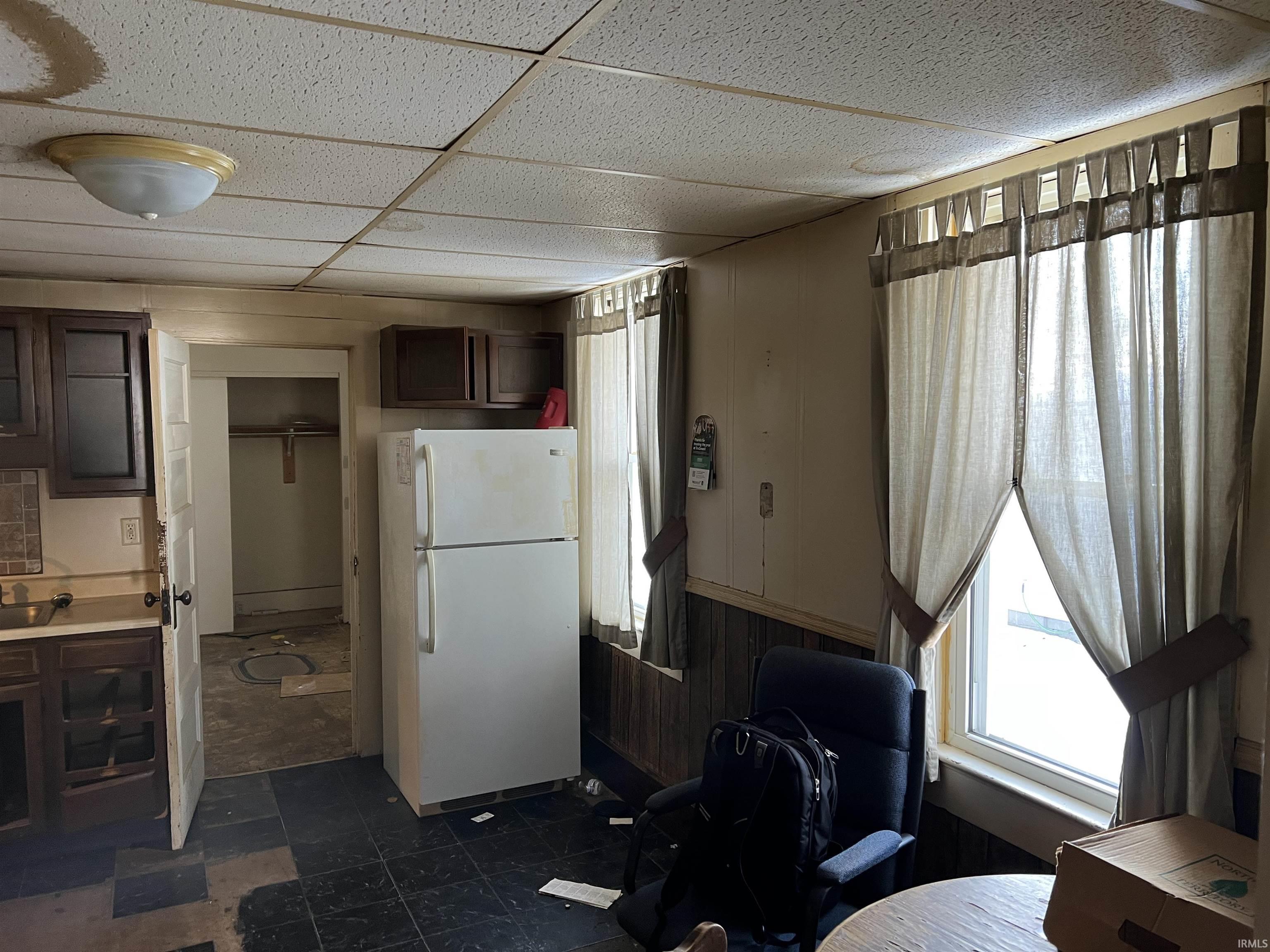 Kitchen featuring a paneled ceiling, freestanding refrigerator, dark brown cabinetry, light countertops, and plenty of natural light
