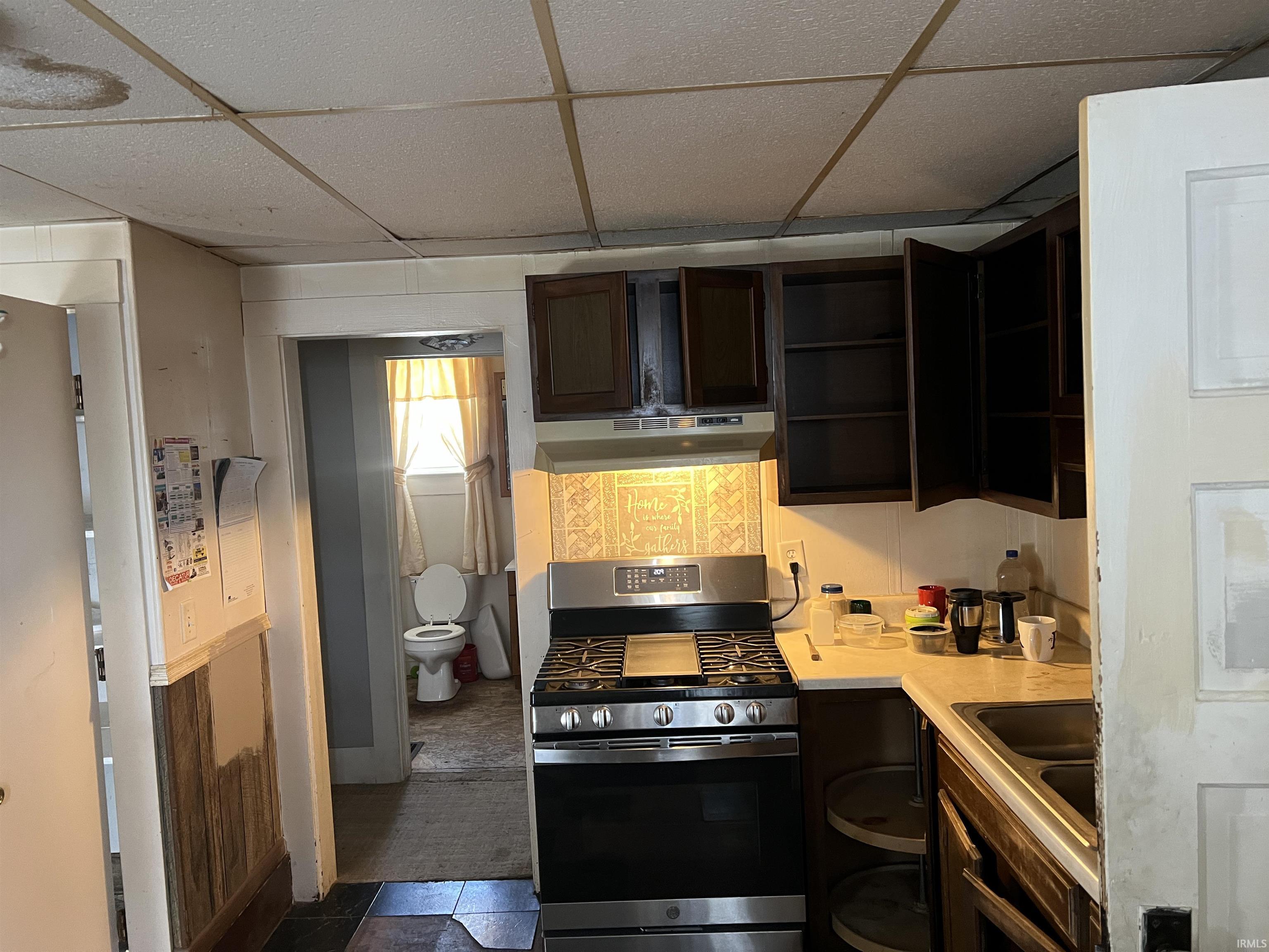Kitchen featuring gas stove, a paneled ceiling, light countertops, dark brown cabinets, and under cabinet range hood