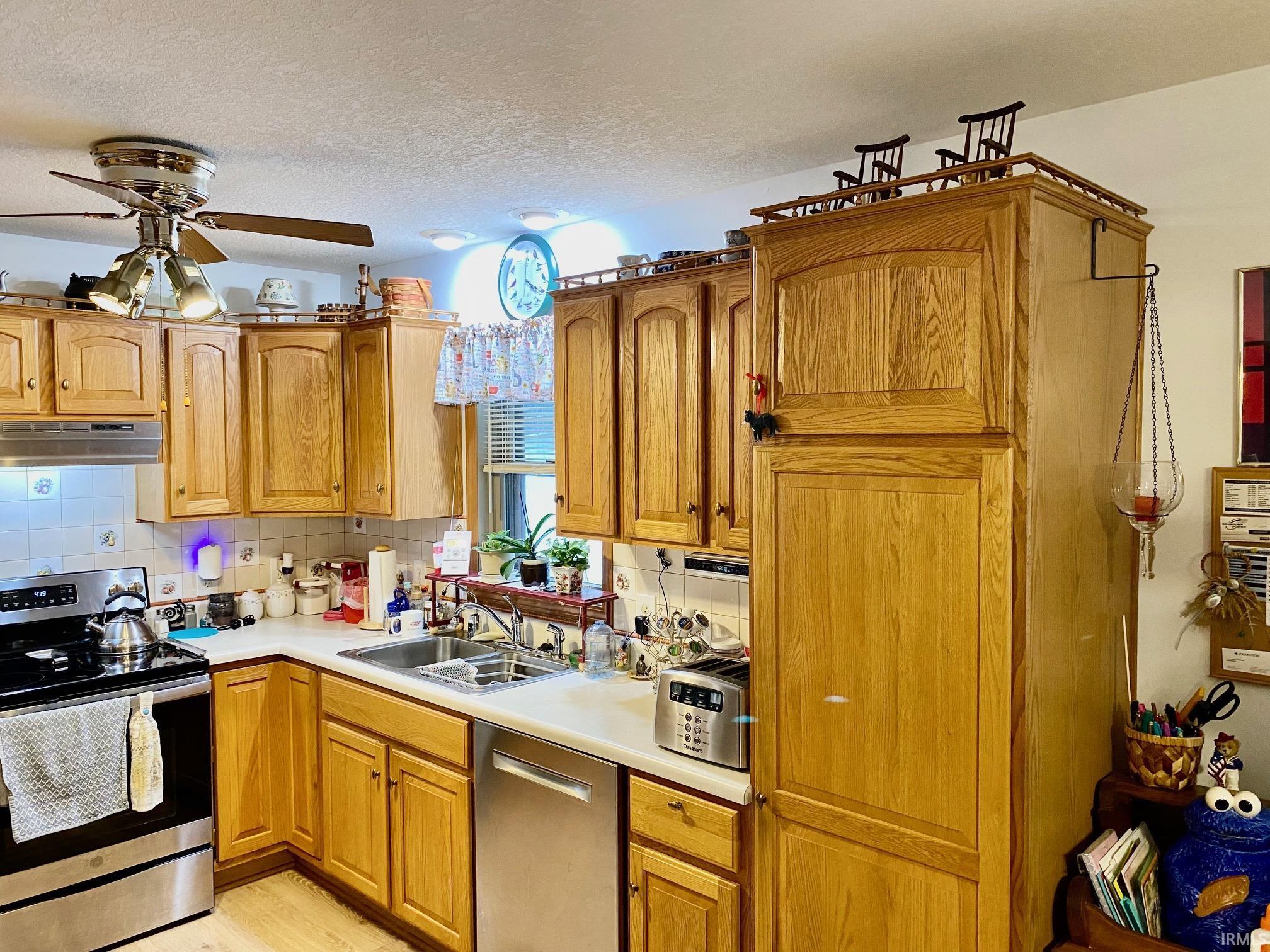 Kitchen with appliances with stainless steel finishes, backsplash, ceiling fan, light countertops, and under cabinet range hood