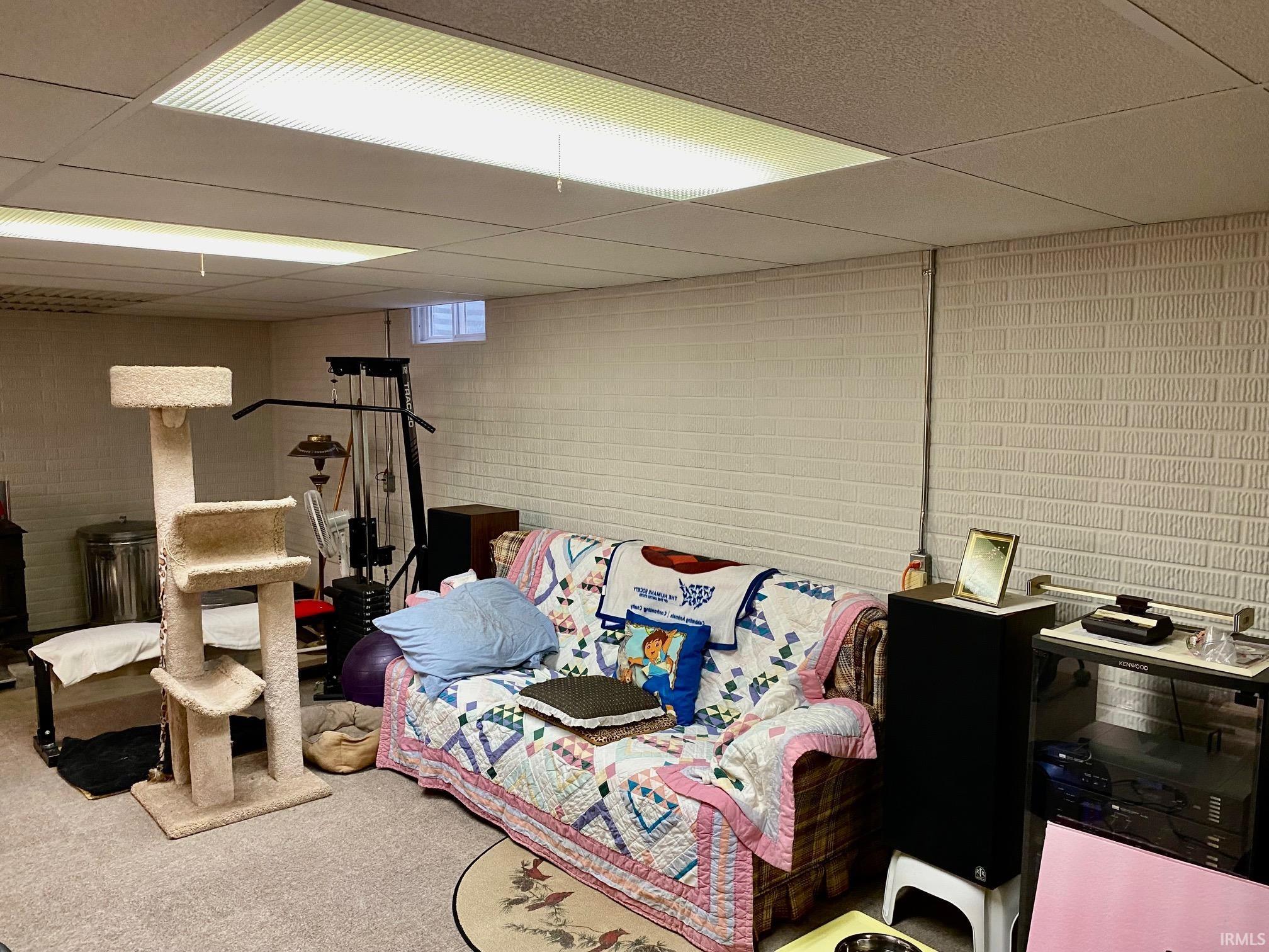 Finished basement with a paneled ceiling, carpet, and concrete block wall