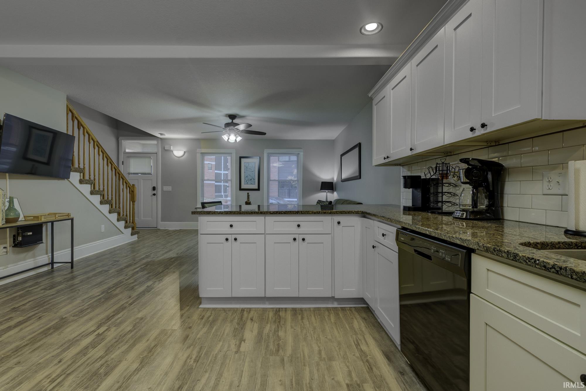 Kitchen with a peninsula, dishwasher, white cabinets, dark stone counters, and light wood finished floors
