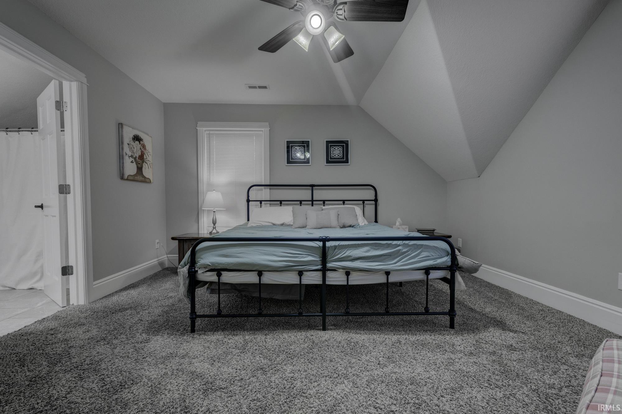 Bedroom with light colored carpet, ceiling fan, ensuite bathroom, and lofted ceiling