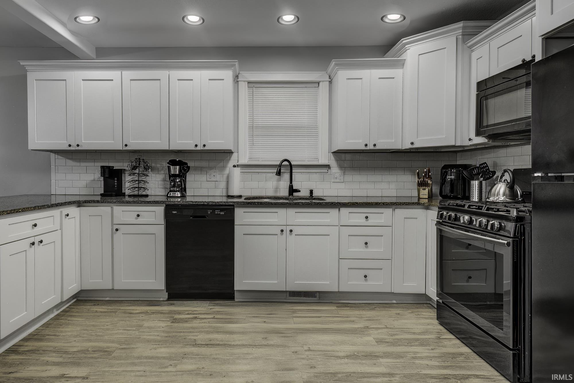 Kitchen with dark stone countertops, black appliances, light wood finished floors, tasteful backsplash, and recessed lighting