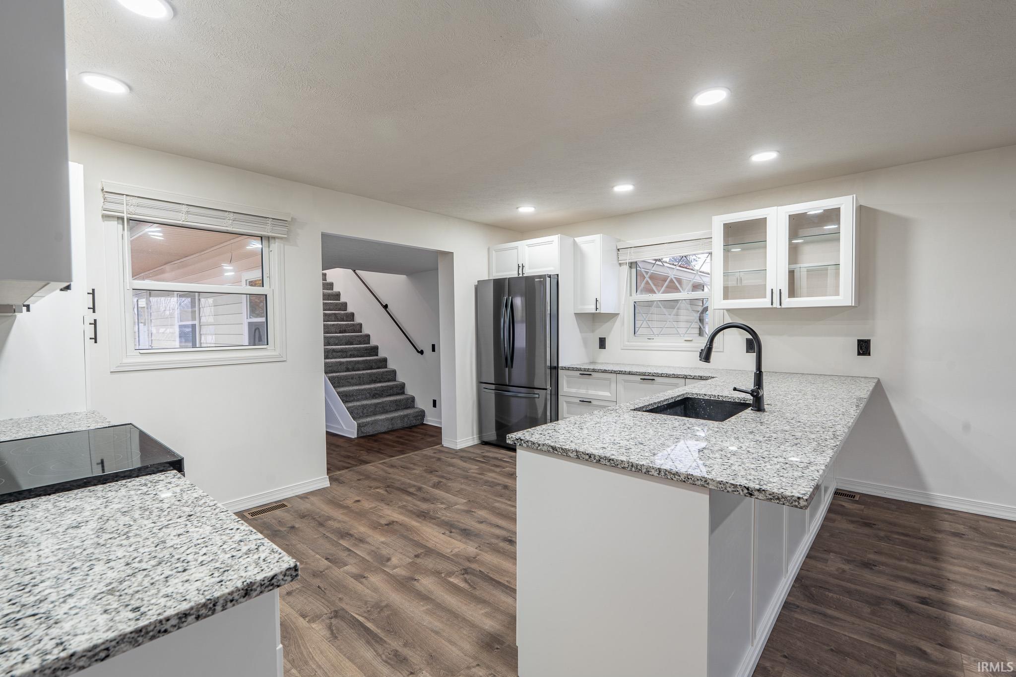 Kitchen featuring light stone countertops, glass insert cabinets, white cabinets, freestanding refrigerator, and a peninsula