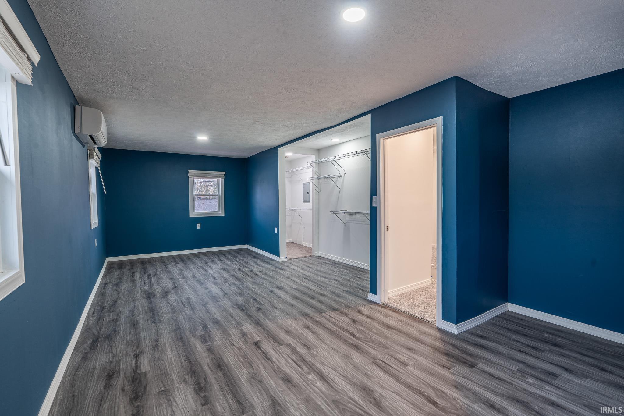 Unfurnished bedroom with a textured ceiling, dark wood-style floors, a walk in closet, a wall mounted air conditioner, and recessed lighting