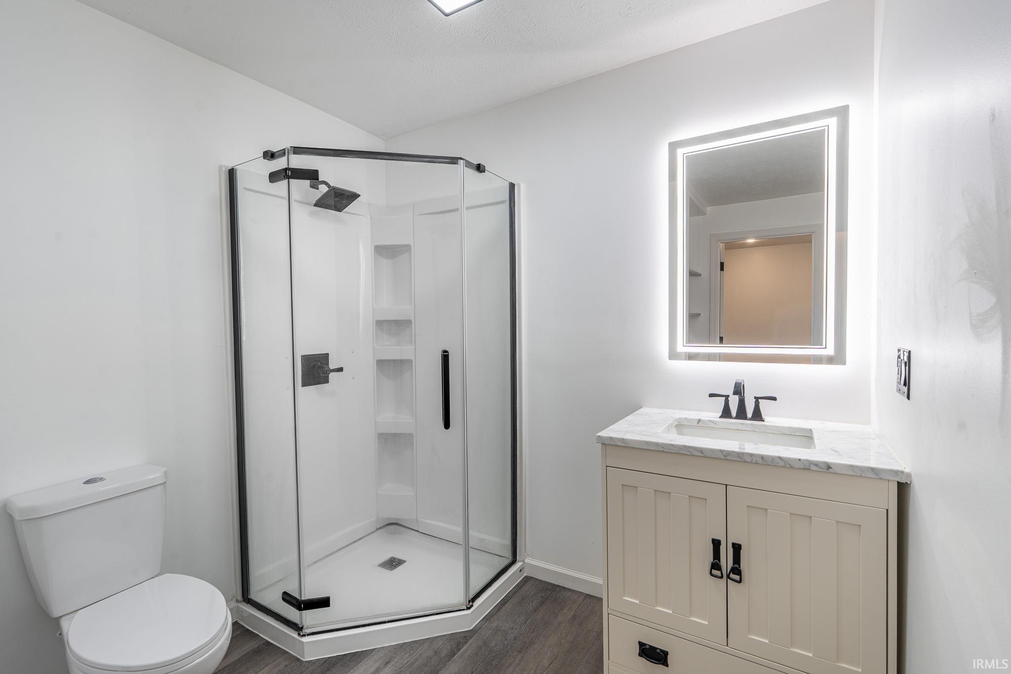 Full bath featuring vanity, a stall shower, and dark wood-style flooring
