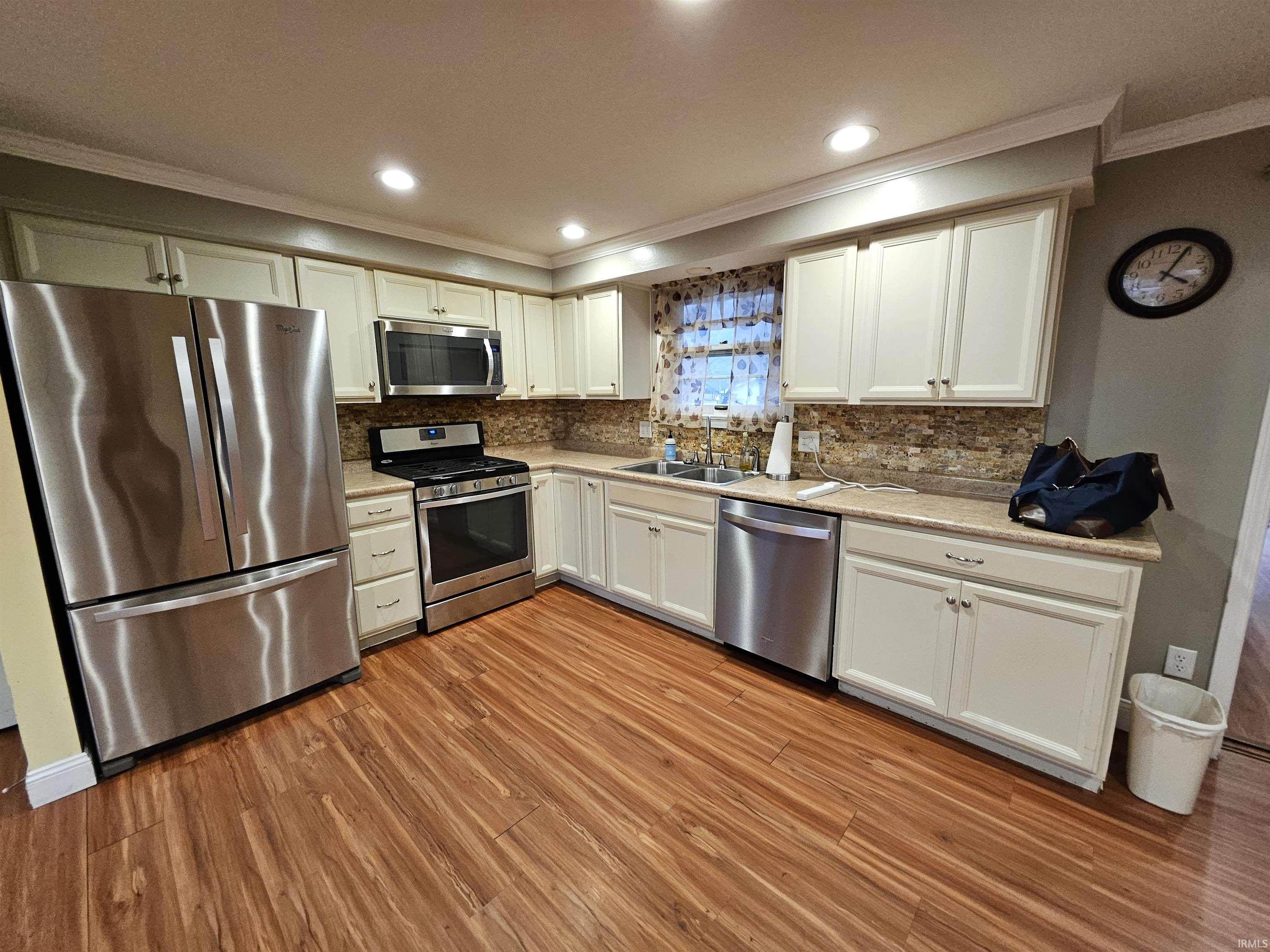 Kitchen with ornamental molding, stainless steel appliances, recessed lighting, white cabinets, and tasteful backsplash