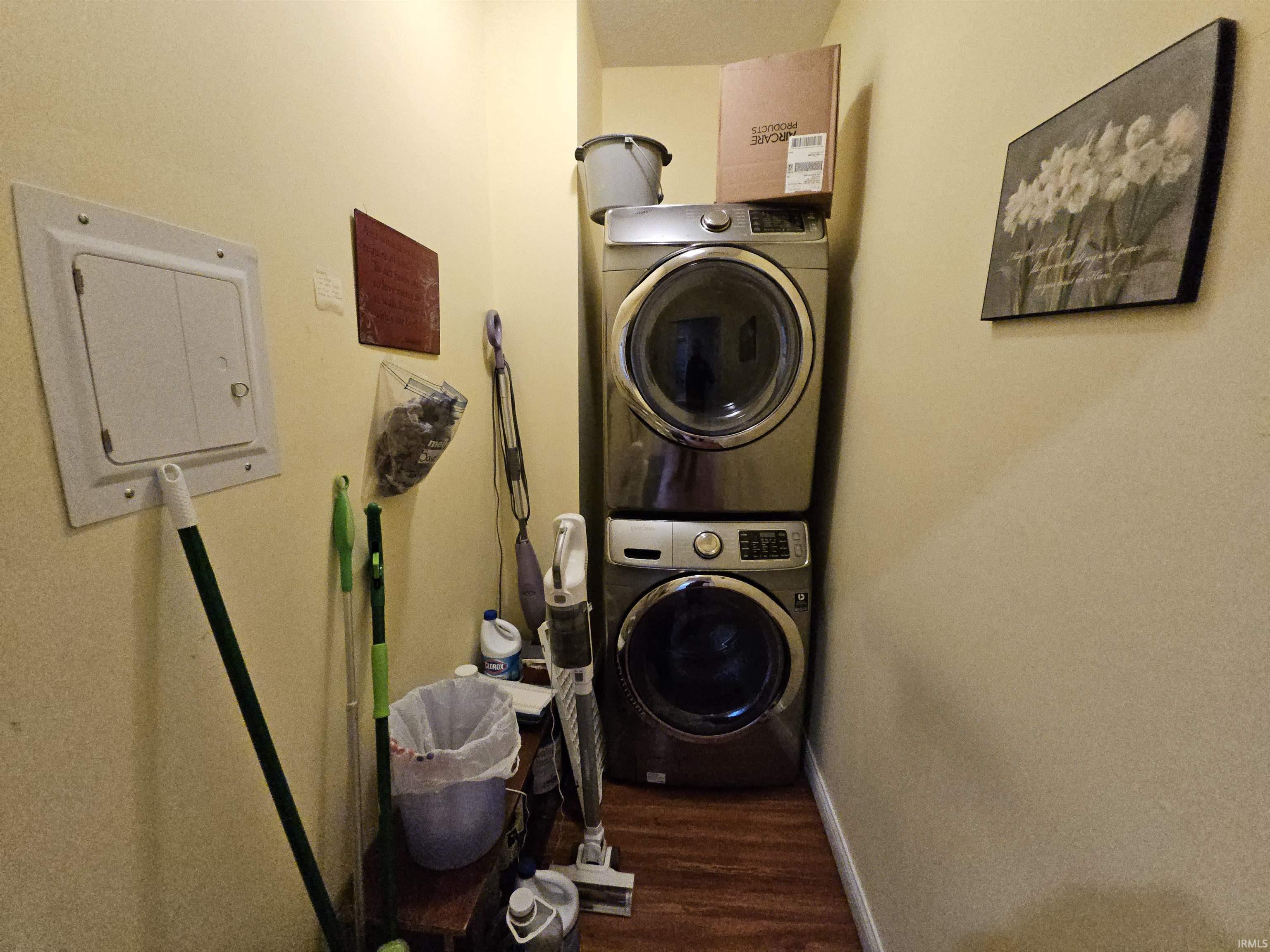 Washroom with electric panel, stacked washing machine and dryer, and dark wood-type flooring