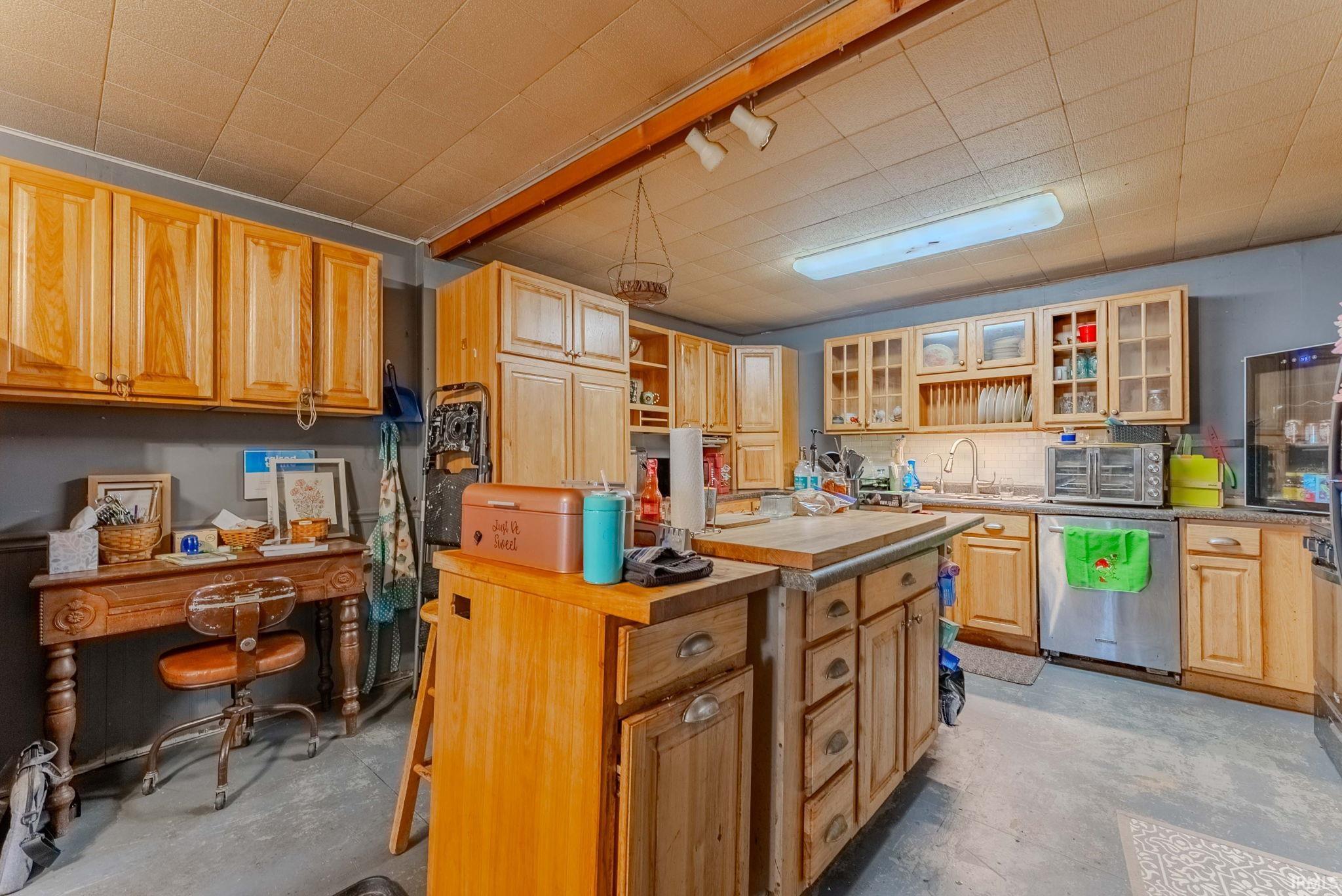 Kitchen featuring glass insert cabinets, unfinished concrete flooring, stainless steel dishwasher, open shelves, and track lighting