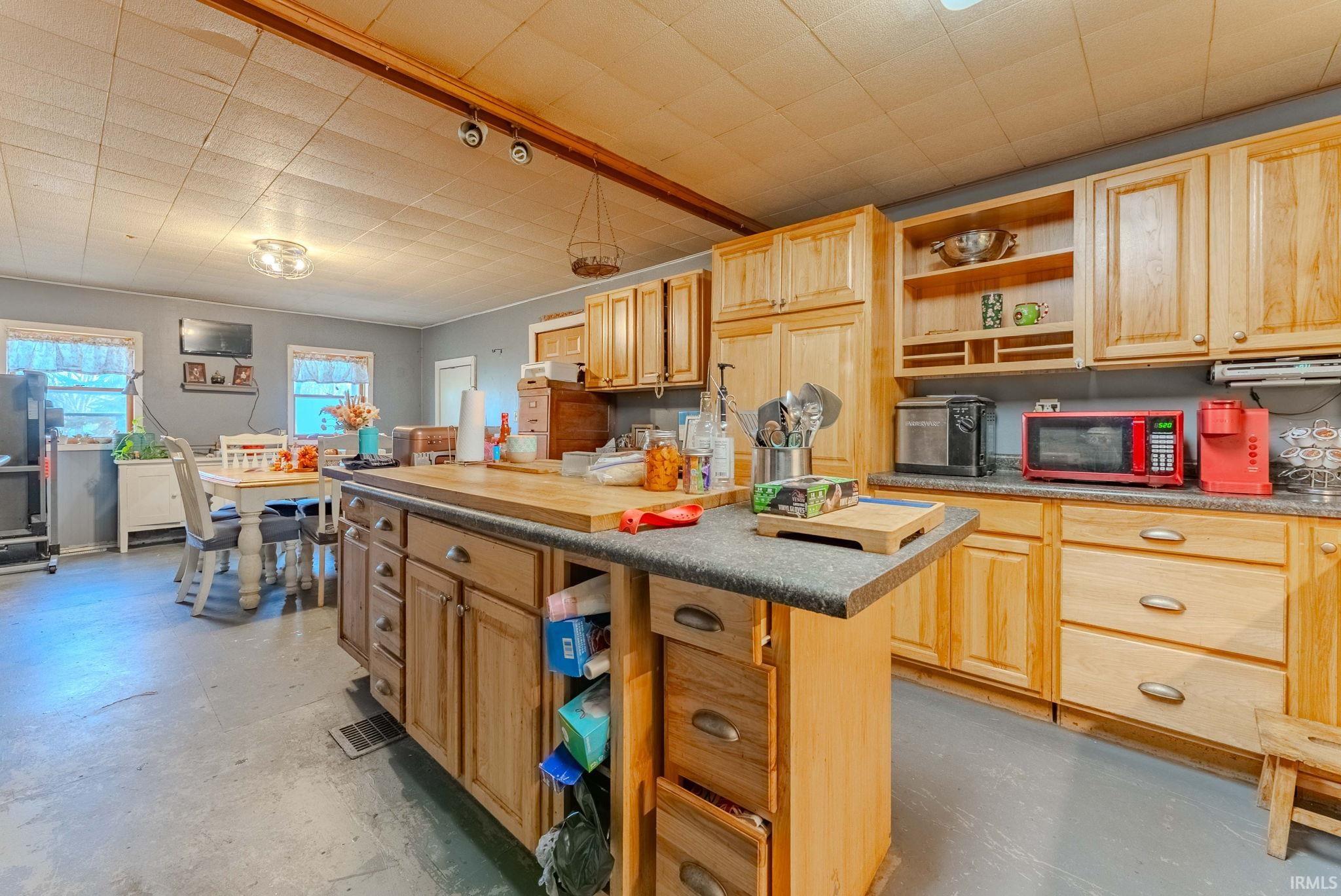 Kitchen with open shelves, light brown cabinetry, dark countertops, and finished concrete flooring