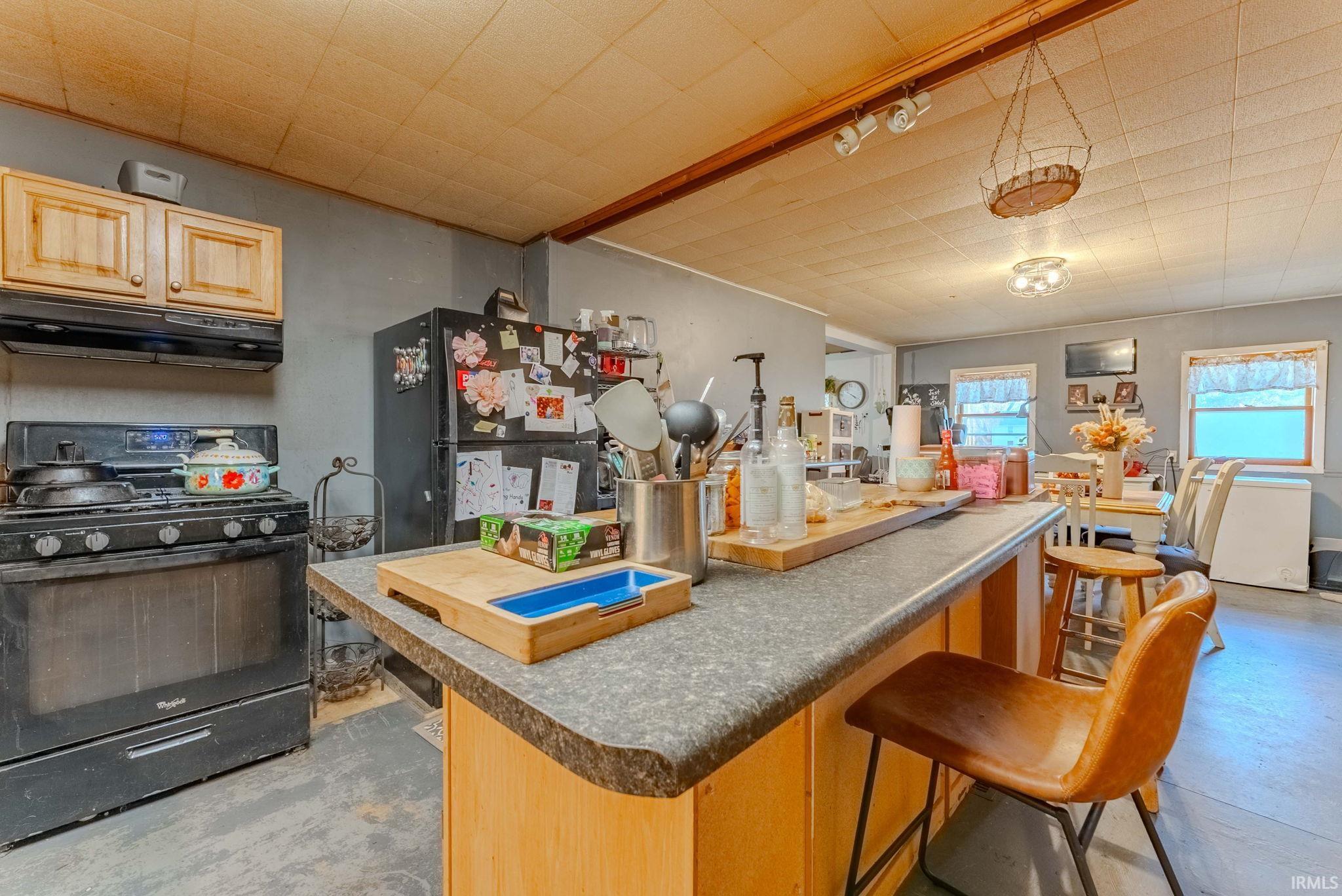 Kitchen with black appliances, a kitchen bar, under cabinet range hood, light brown cabinets, and a center island