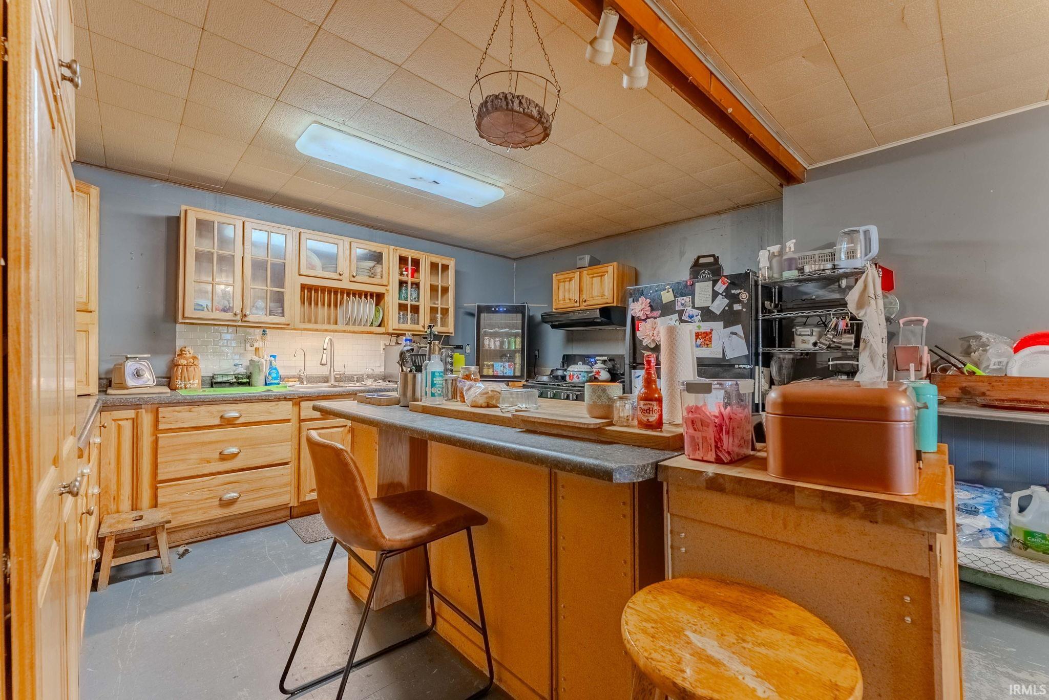 Kitchen with a breakfast bar area, glass insert cabinets, tasteful backsplash, and light brown cabinetry