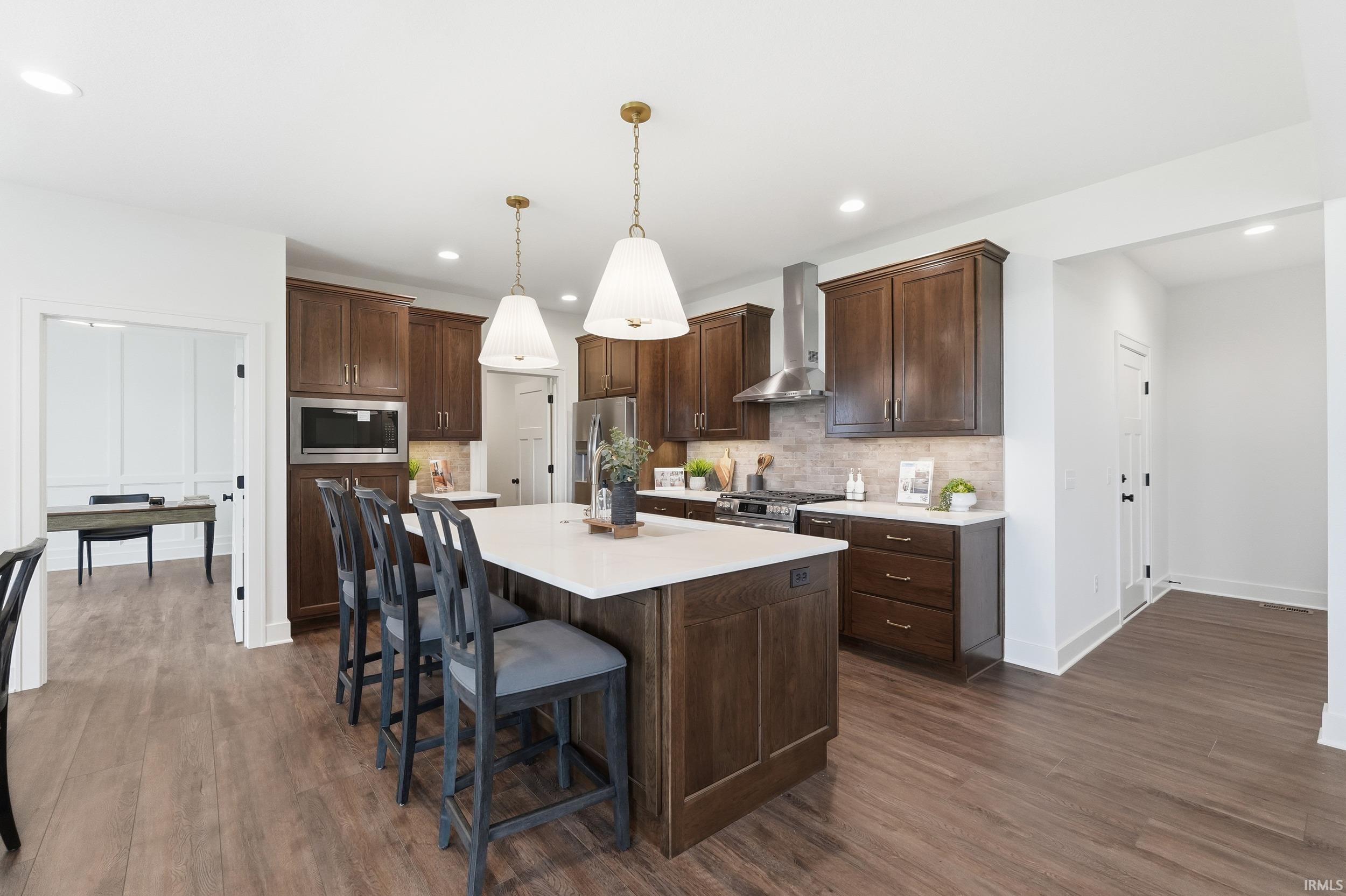 Kitchen with a kitchen breakfast bar, hanging light fixtures, decorative backsplash, dark brown cabinets, and recessed lighting