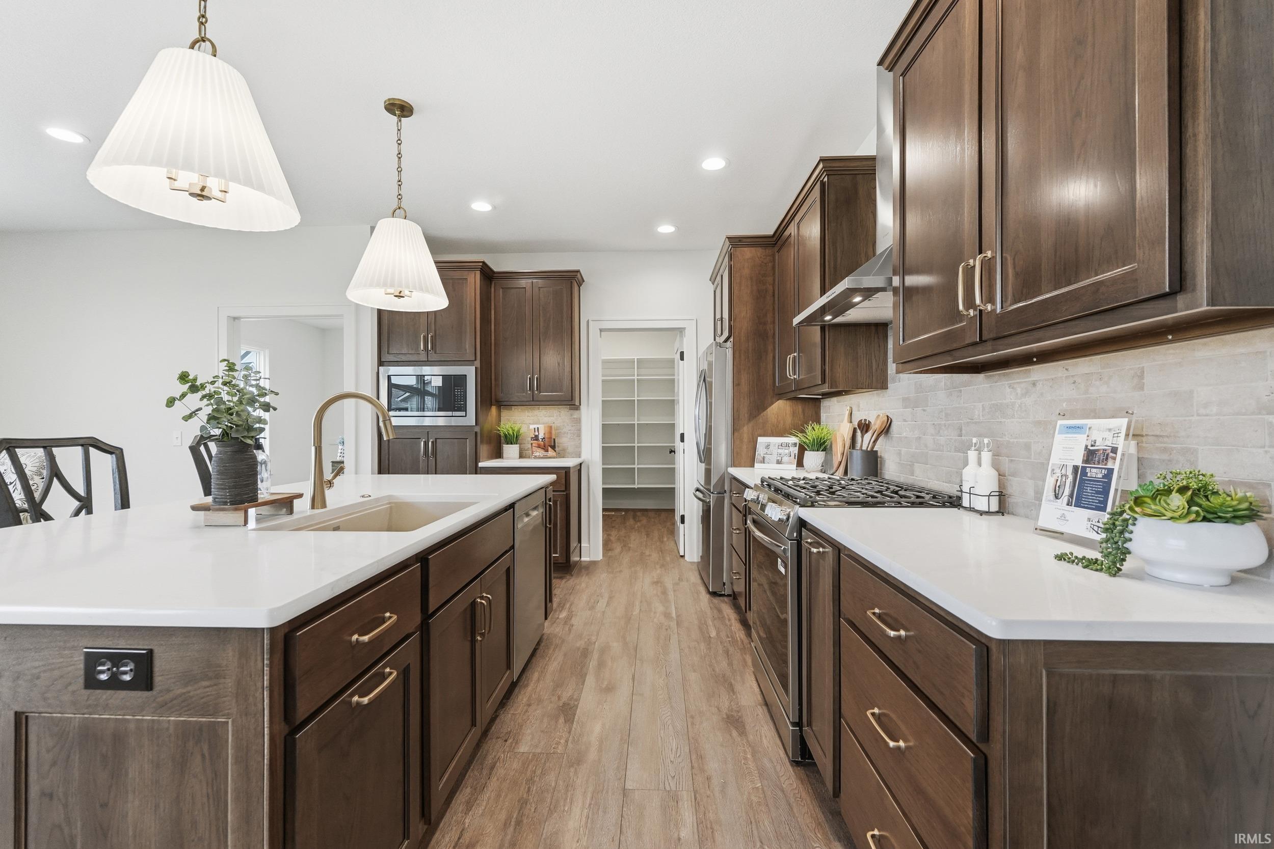 Kitchen with dark brown cabinets, a center island with sink, decorative light fixtures, tasteful backsplash, and light wood-style flooring