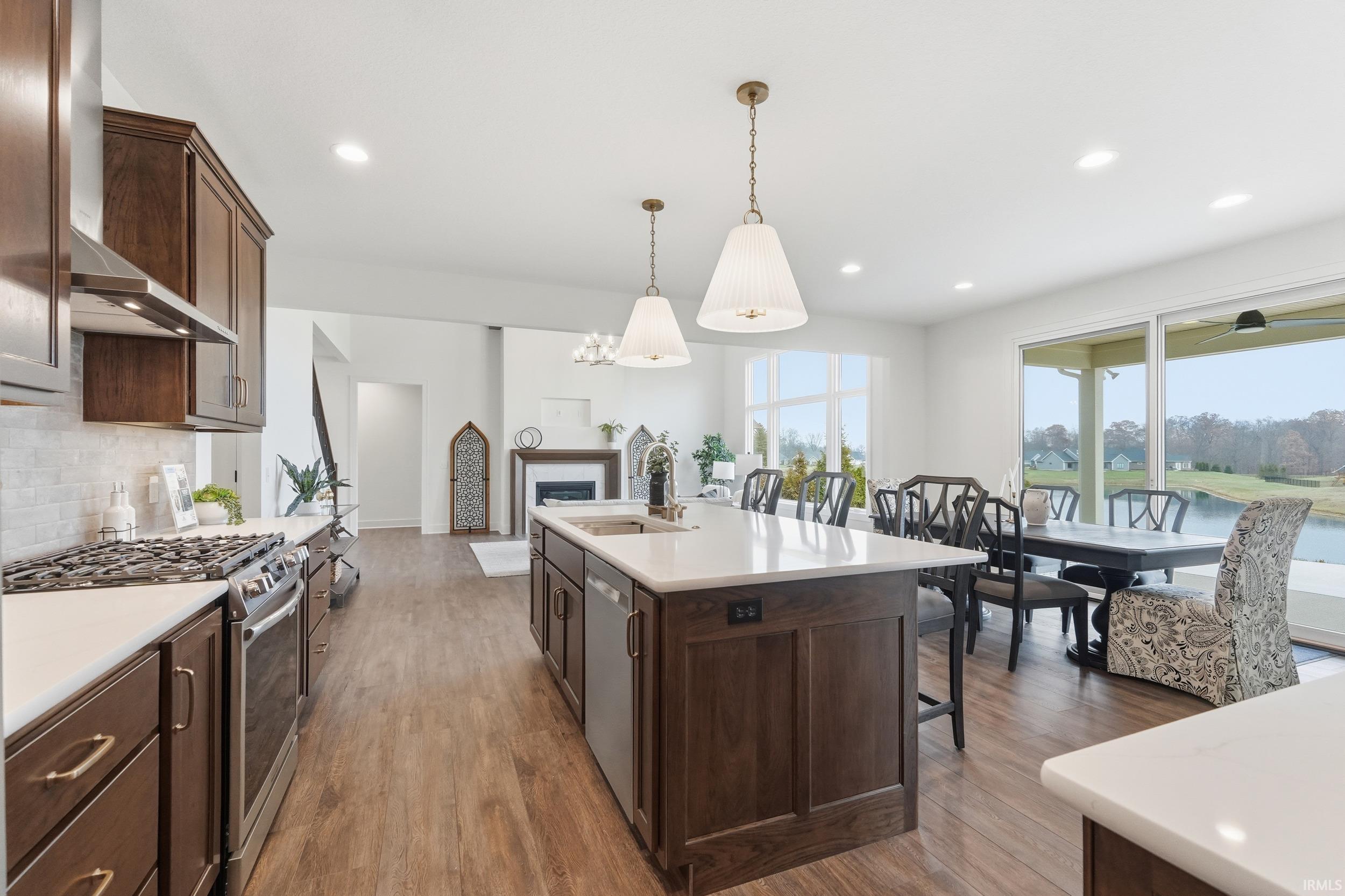 Kitchen with dark brown cabinets, appliances with stainless steel finishes, light wood finished floors, wall chimney exhaust hood, and tasteful backsplash